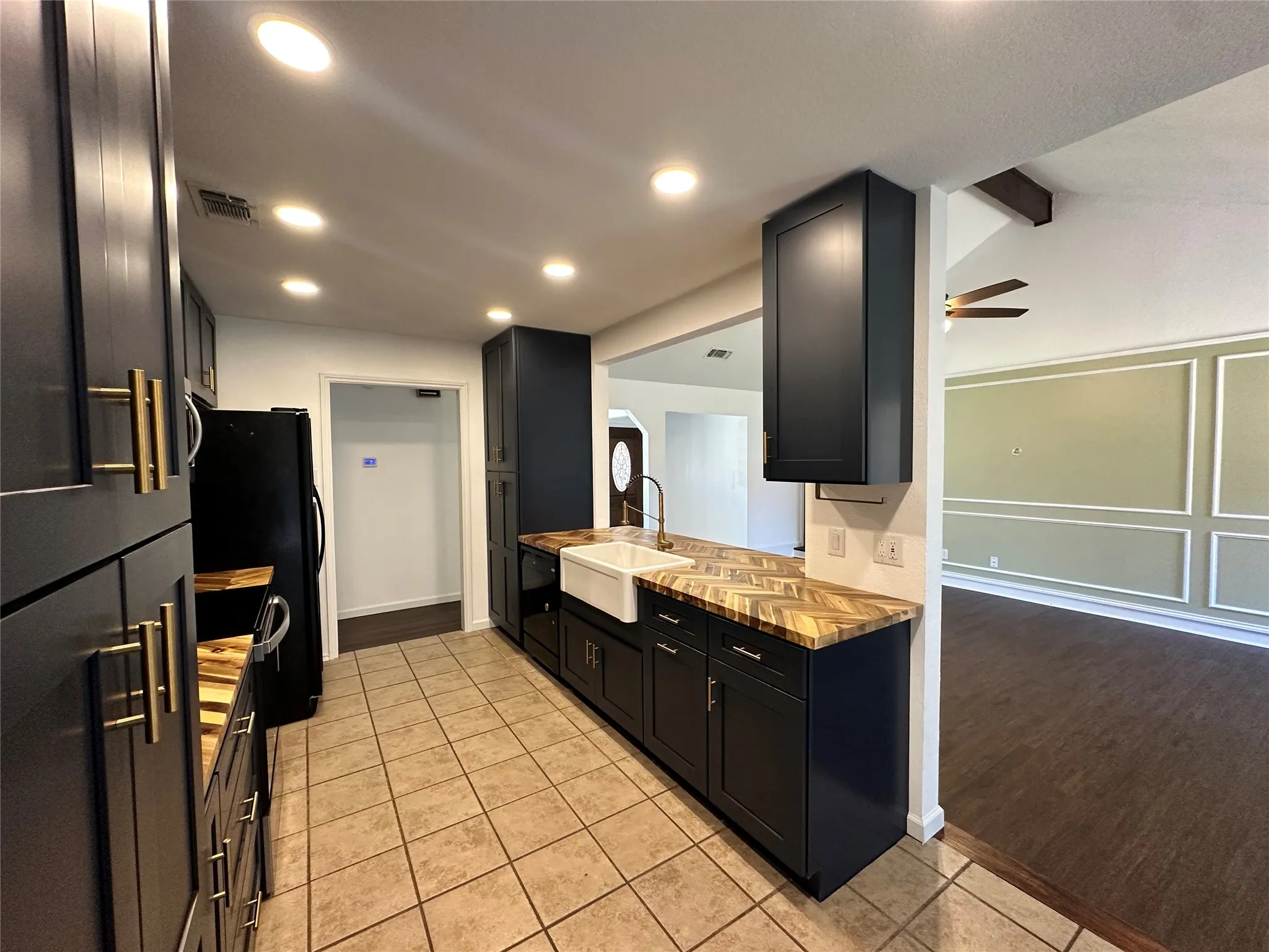 Kitchen featuring dark cabinetry with gold-tone hardware, wood-finish countertops, a farmhouse-style sink with a gooseneck faucet, and recessed lighting