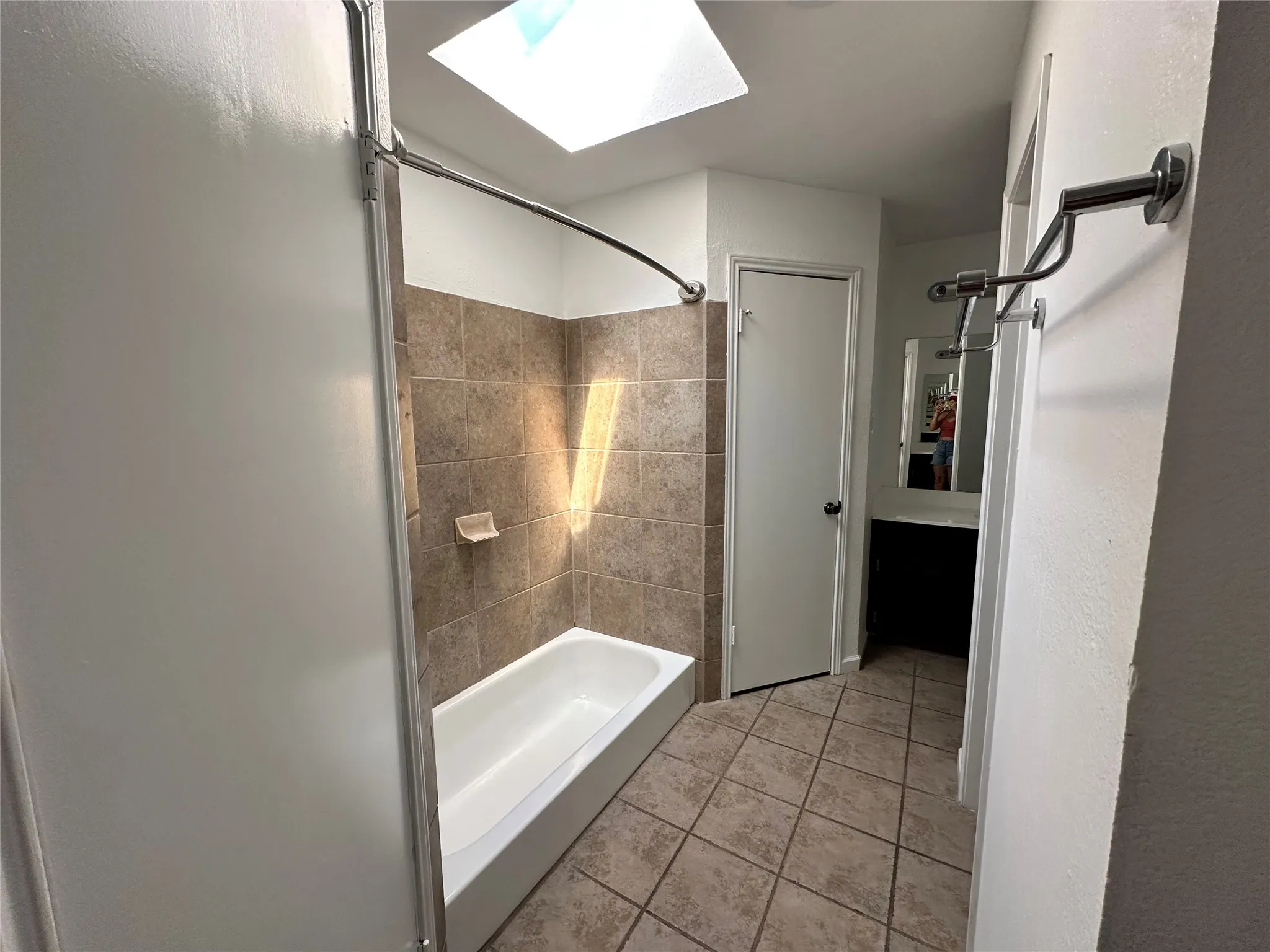 Bathroom featuring a skylight, tile flooring, a built-in bathtub with tile surround, a dark wood-finish vanity, and a wall-mounted mirror
