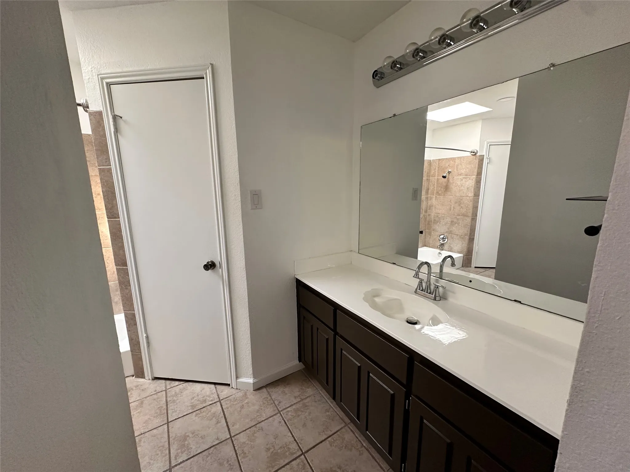 Vanity with an integrated sink, wall to wall mirror, ample counter and storage space, and a chrome light fixture