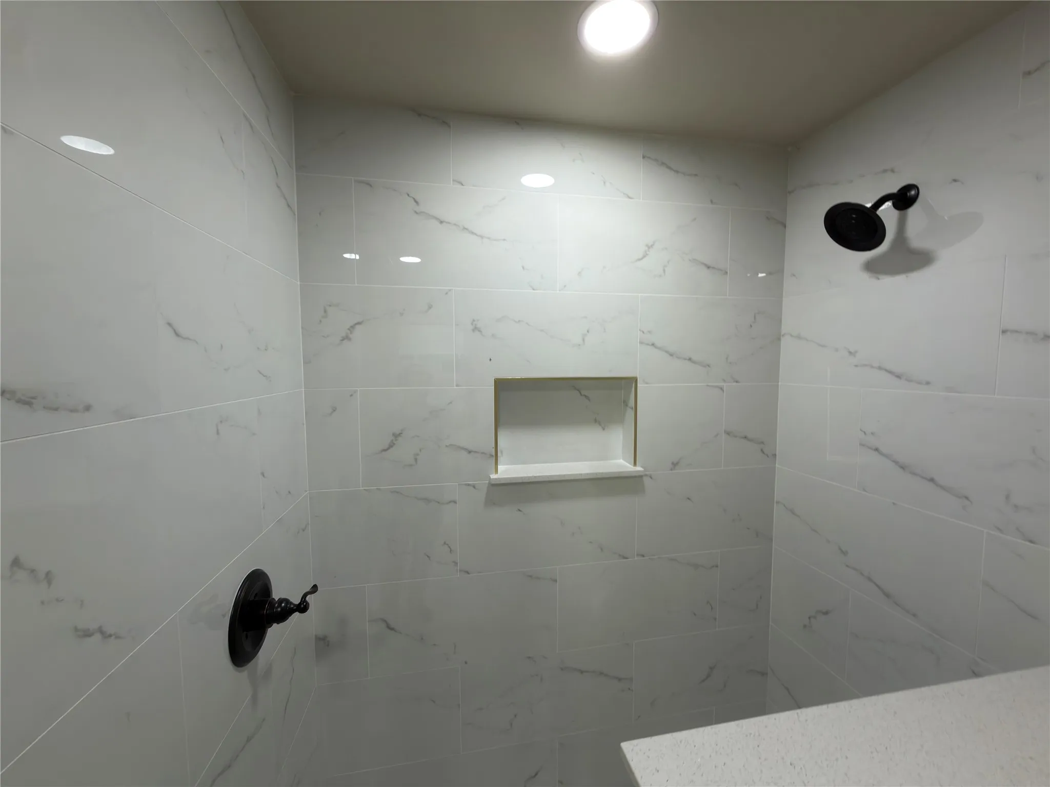 Shower featuring white tile with gray veining, a built-in shower niche, matte black shower fixtures, and recessed lighting