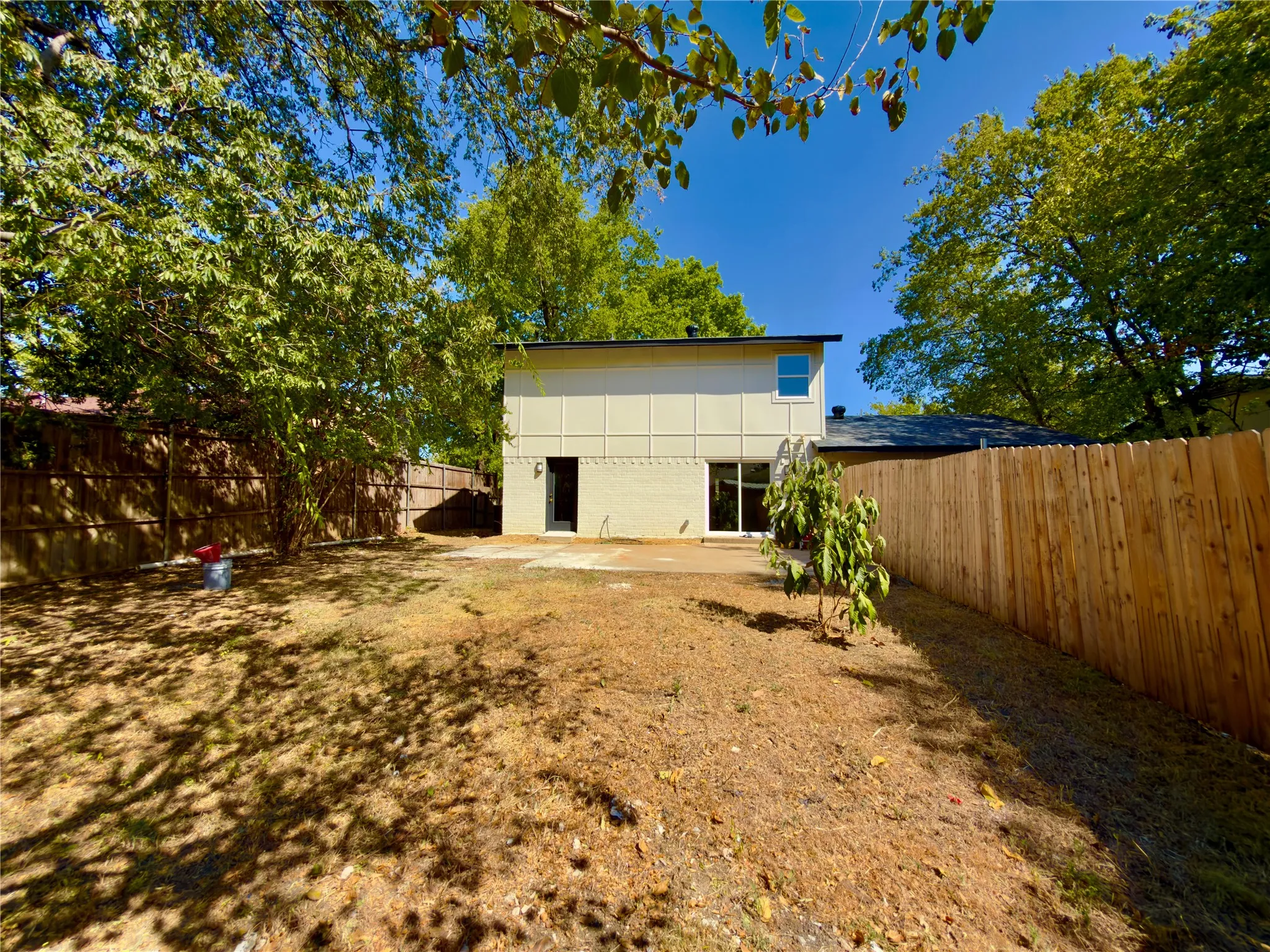 Expansive yard with mature trees, offering privacy with full wood fencing