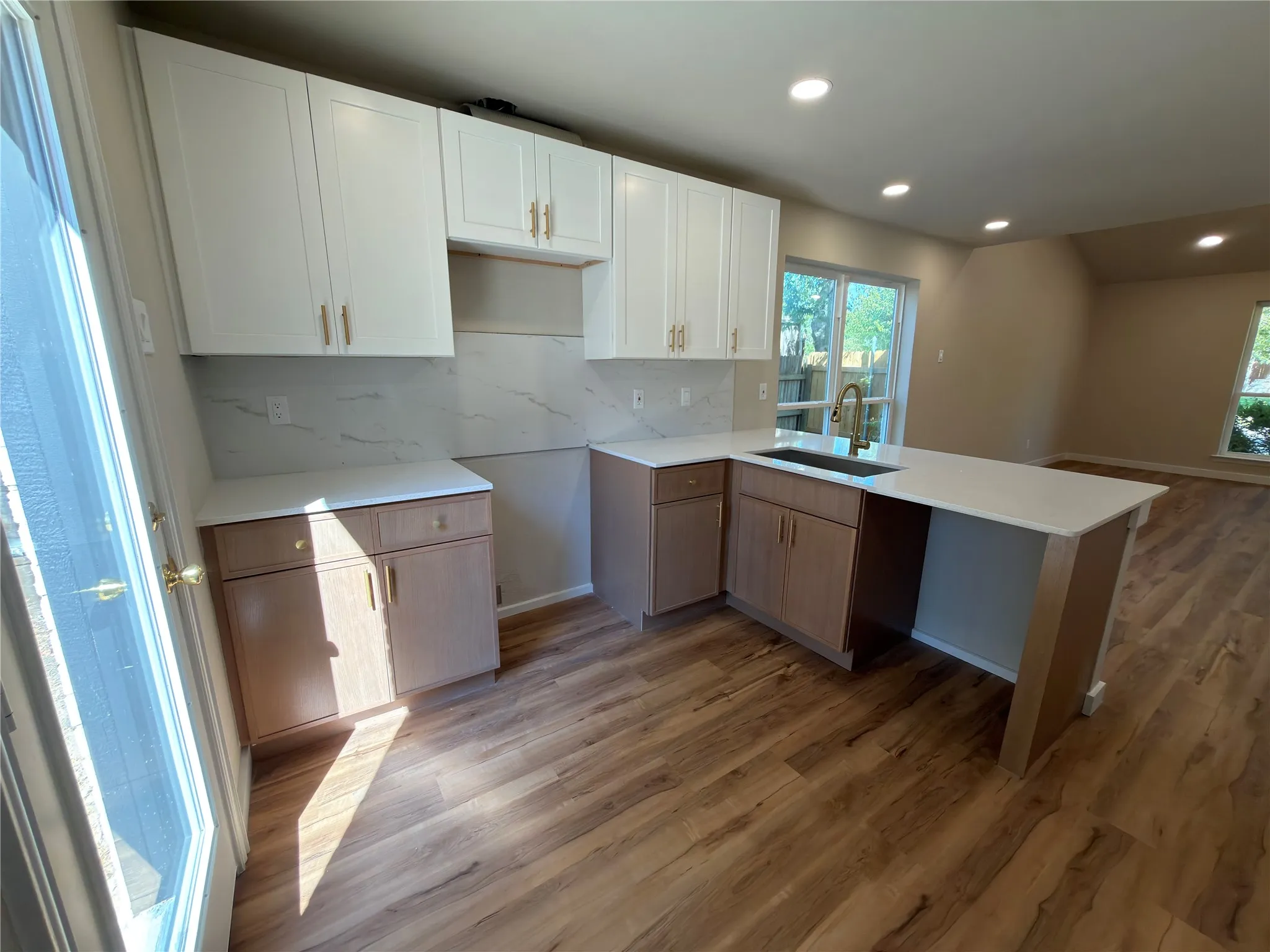 Modern kitchen featuring white upper cabinetry, wood-finish lower cabinetry, light-toned countertops, a white tile backsplash, and wood-finish flooring