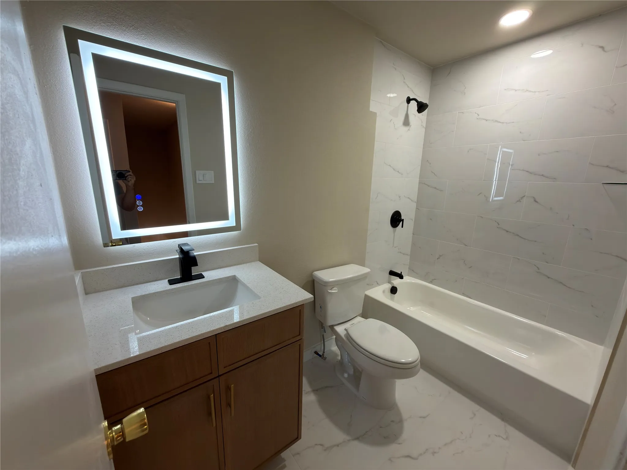 Bathroom featuring a wood-finish vanity with a light-colored countertop, integrated sink, and matte black faucet