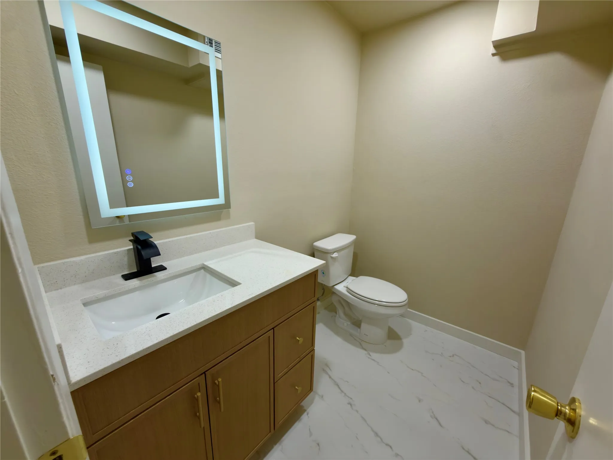 Vanity with integrated sink, modern black faucet, illuminated mirror, and marble-look flooring