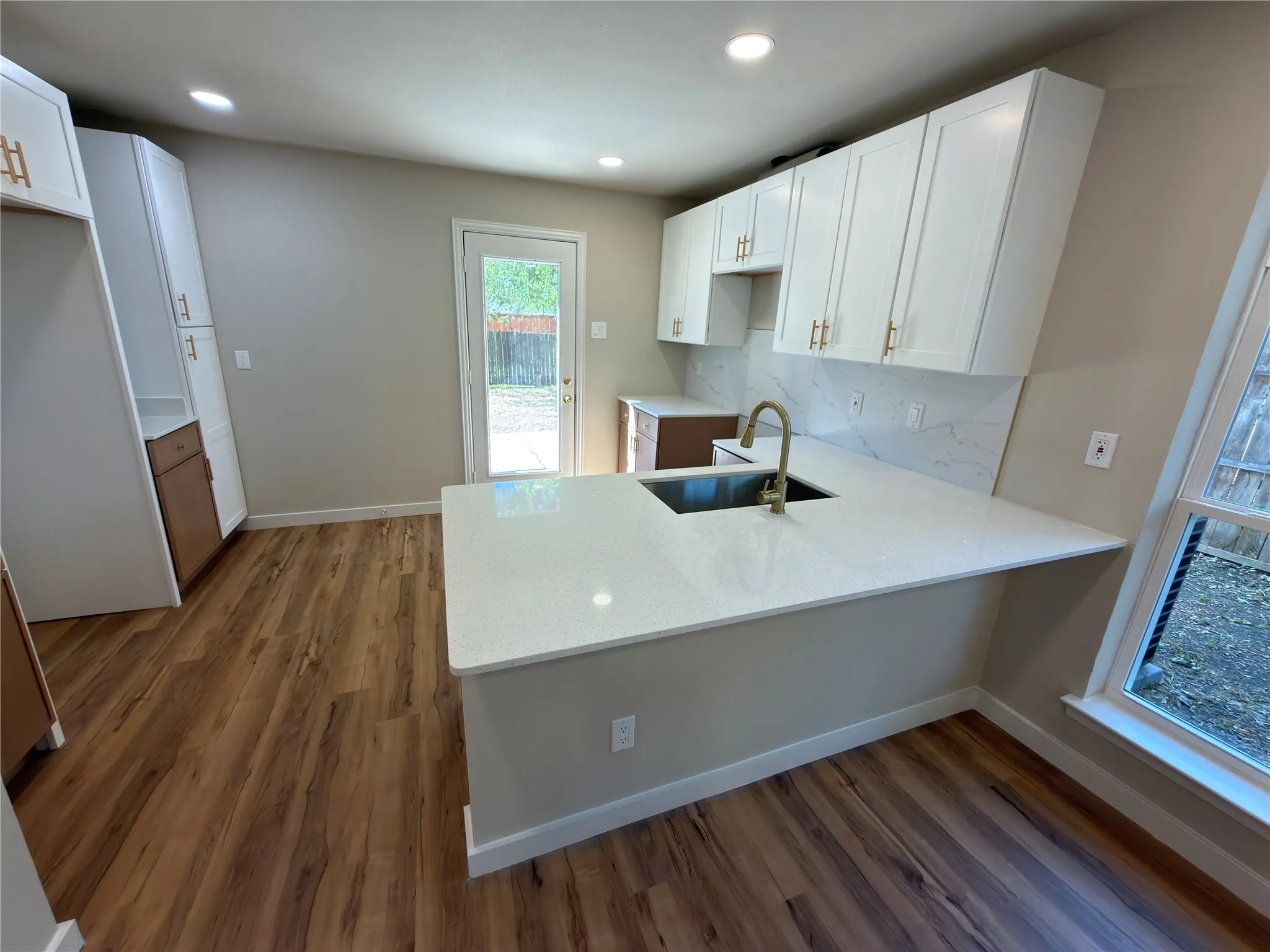 Kitchen featuring white shaker cabinetry, wood-finish flooring, recessed lighting, a kitchen island with an undermount sink, and a full backsplash