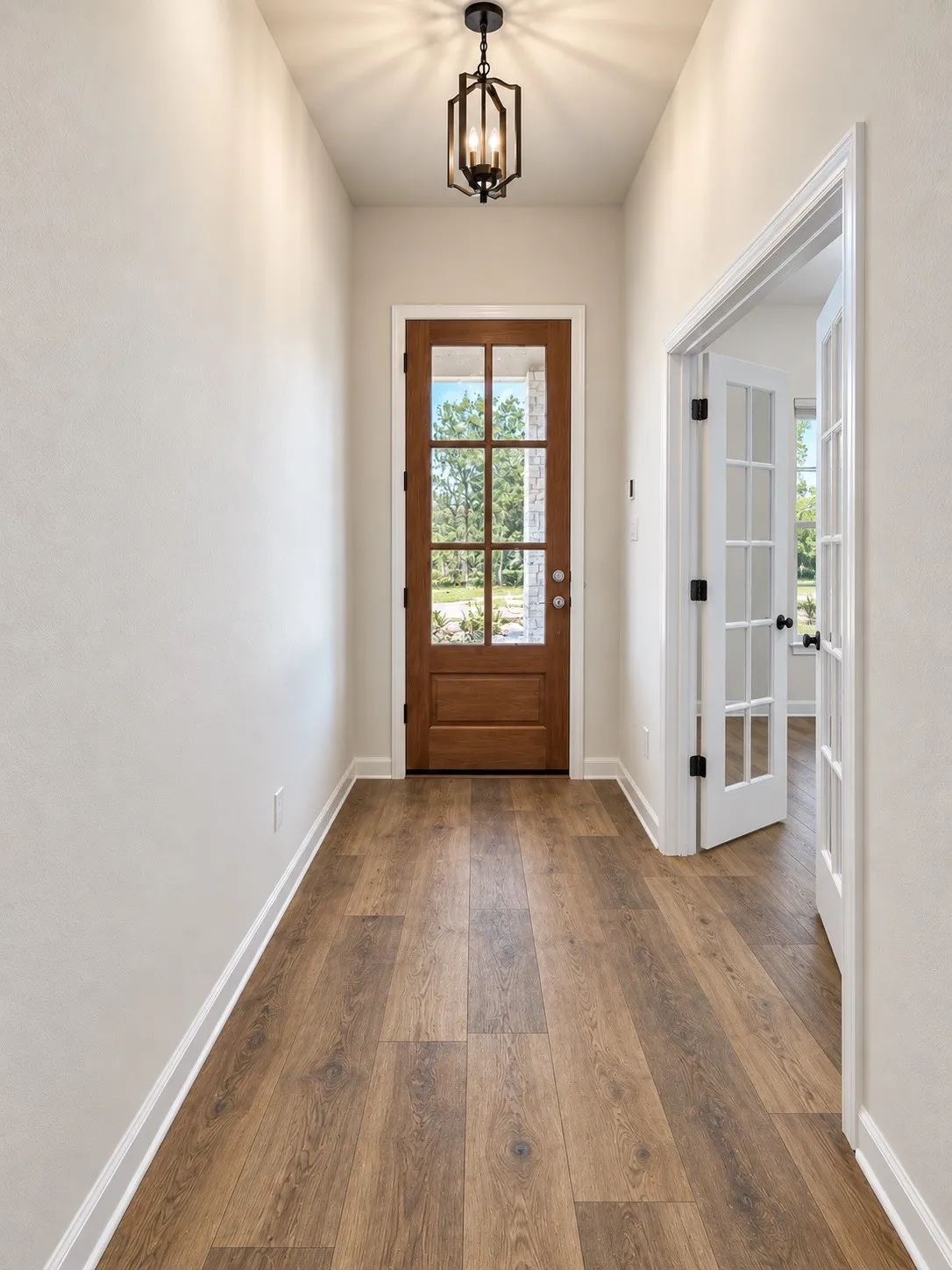 Wood-finish flooring, a wood entry door with divided lites, an exposed beam chandelier, and a white framed doorway with French doors