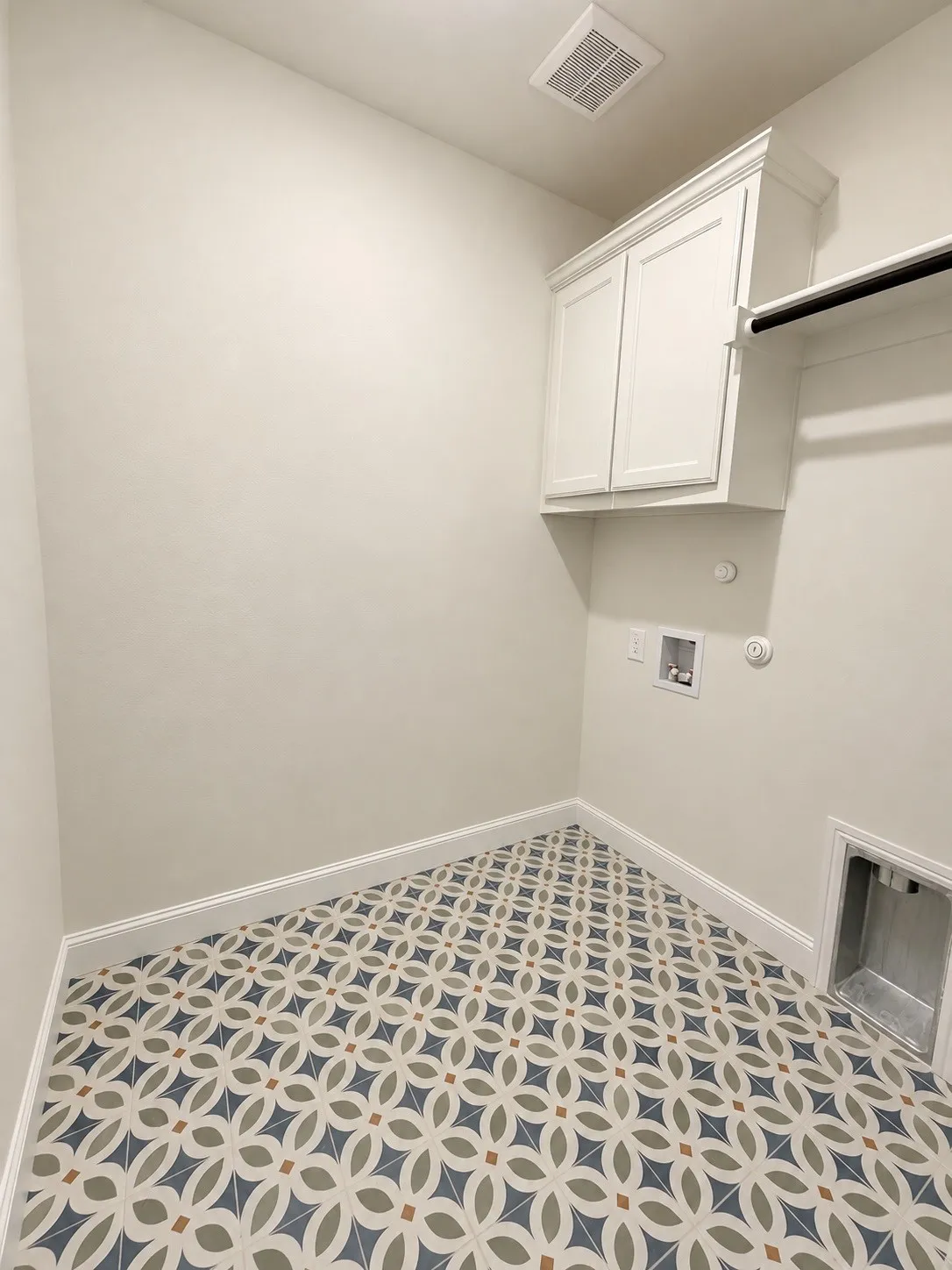 Laundry area featuring patterned tile flooring, white shaker-style cabinetry, and a clothes hanging rod