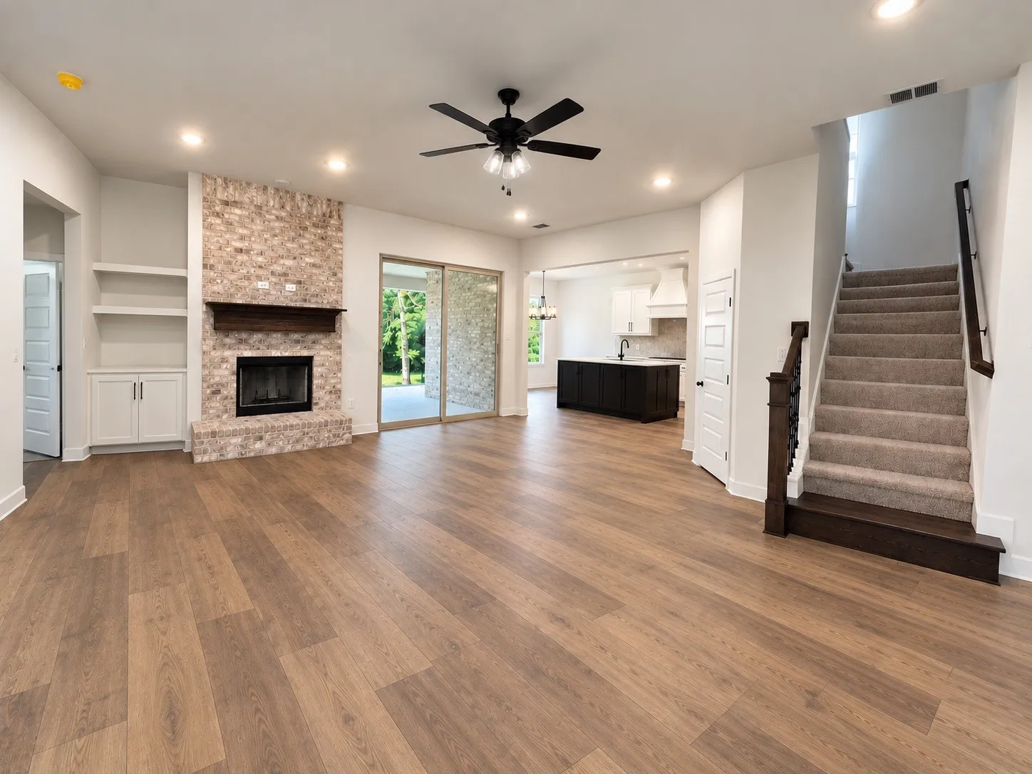 Wood-finish flooring throughout, brick fireplace with wood mantel, built-in shelving with lower cabinetry, sliding glass doors, and recessed lighting