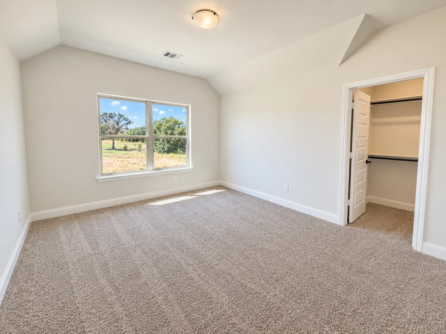 Vaulted ceiling bedroom featuring carpeting, a multi-pane window, and a built-in closet with shelving