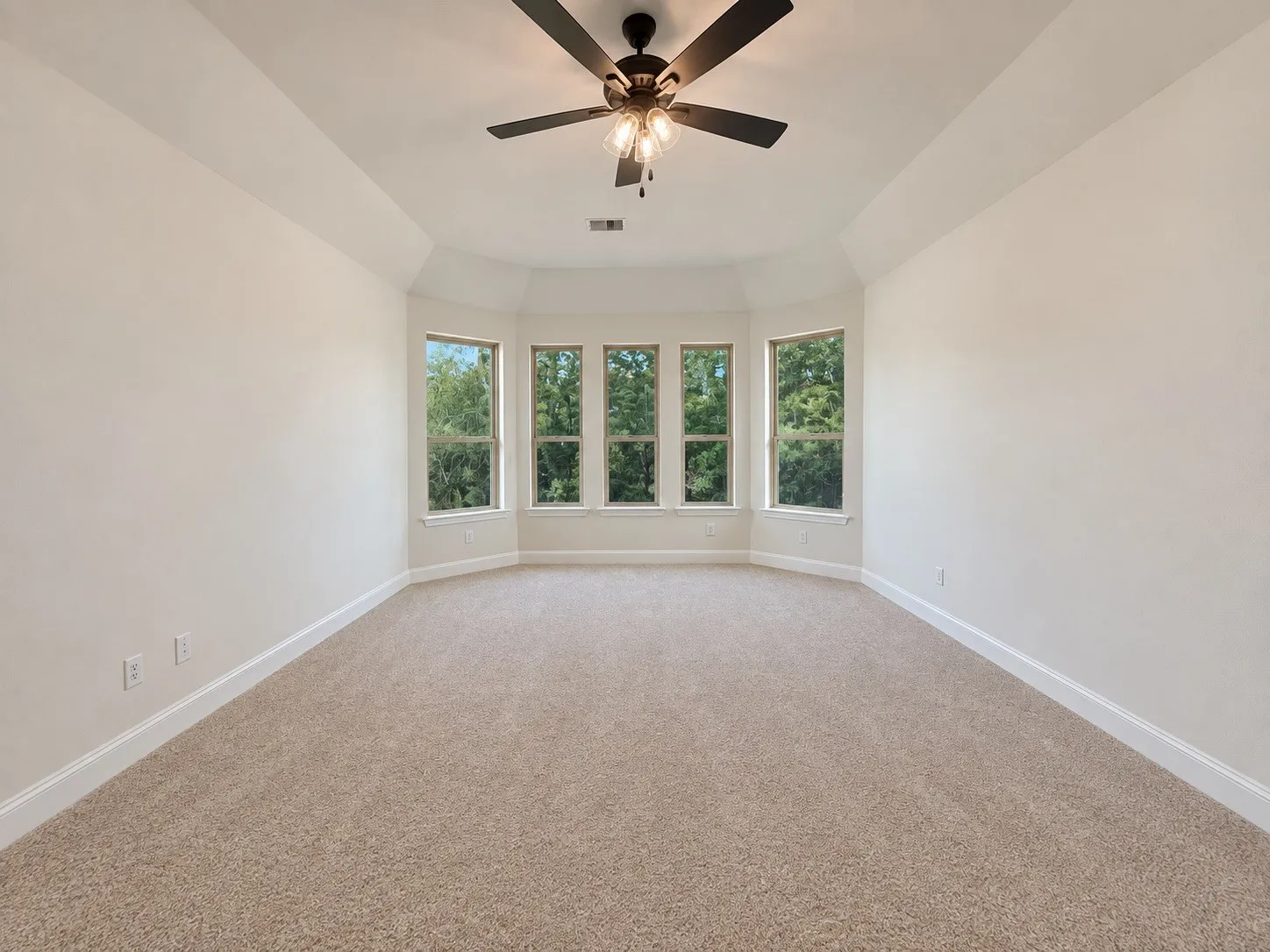Carpeted interior space featuring a multi-window bay, tray ceiling, and a ceiling fan with integrated lighting