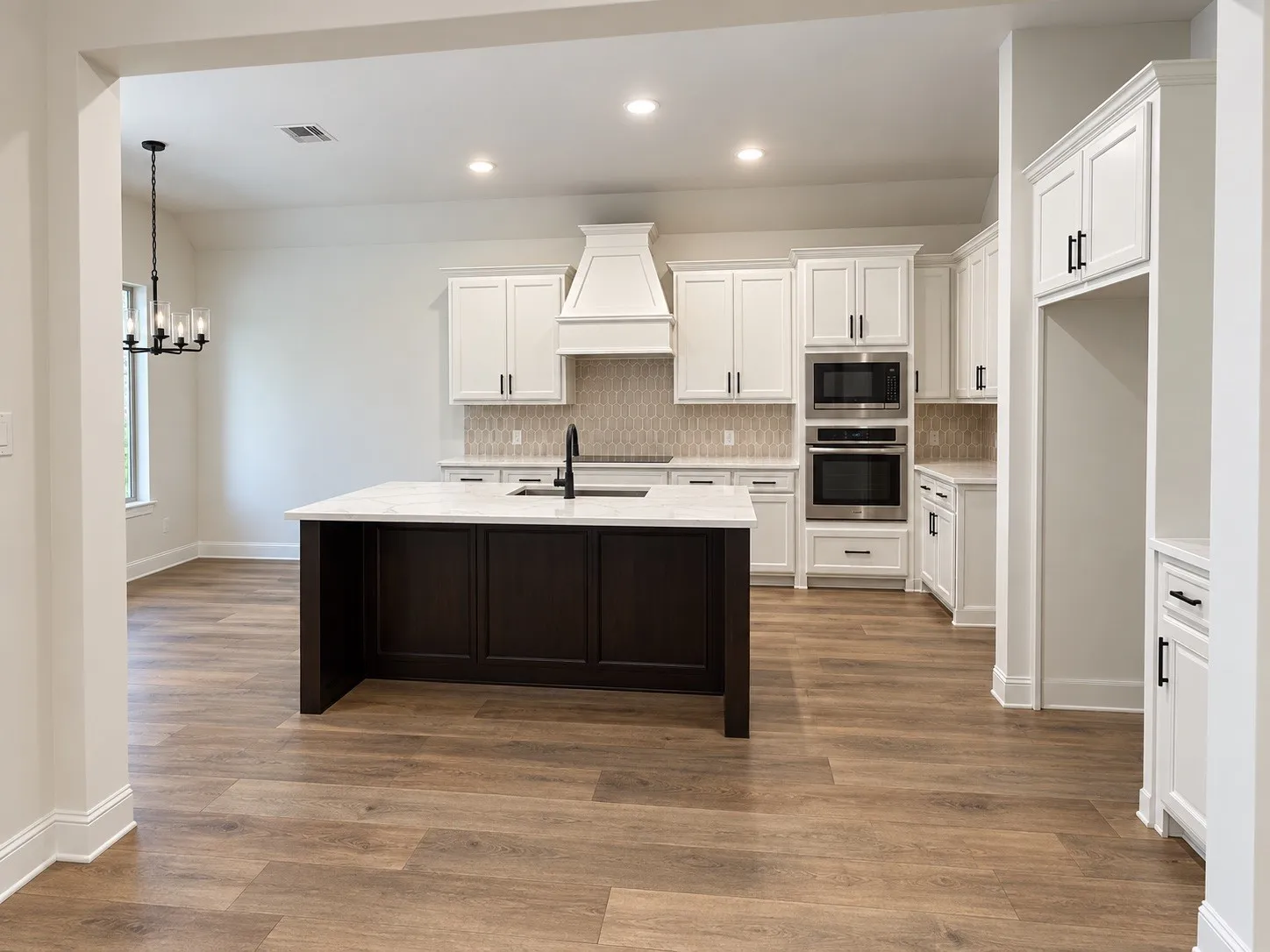 Kitchen featuring a central island with a contrasting dark wood finish, white cabinetry, integrated stainless steel appliances, and wood-finish flooring