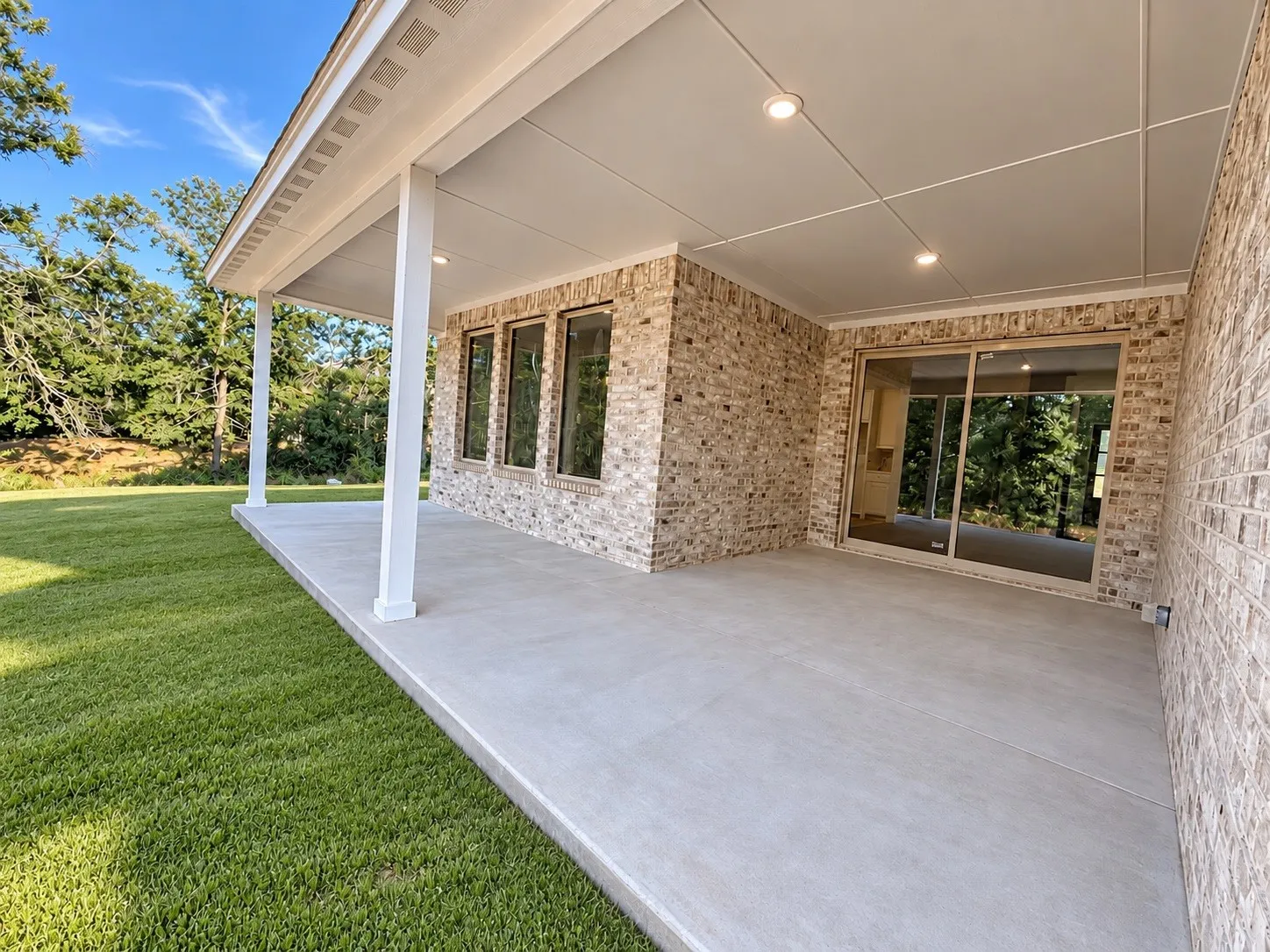 Expansive covered patio with recessed lighting, brick exterior, and a sliding glass door