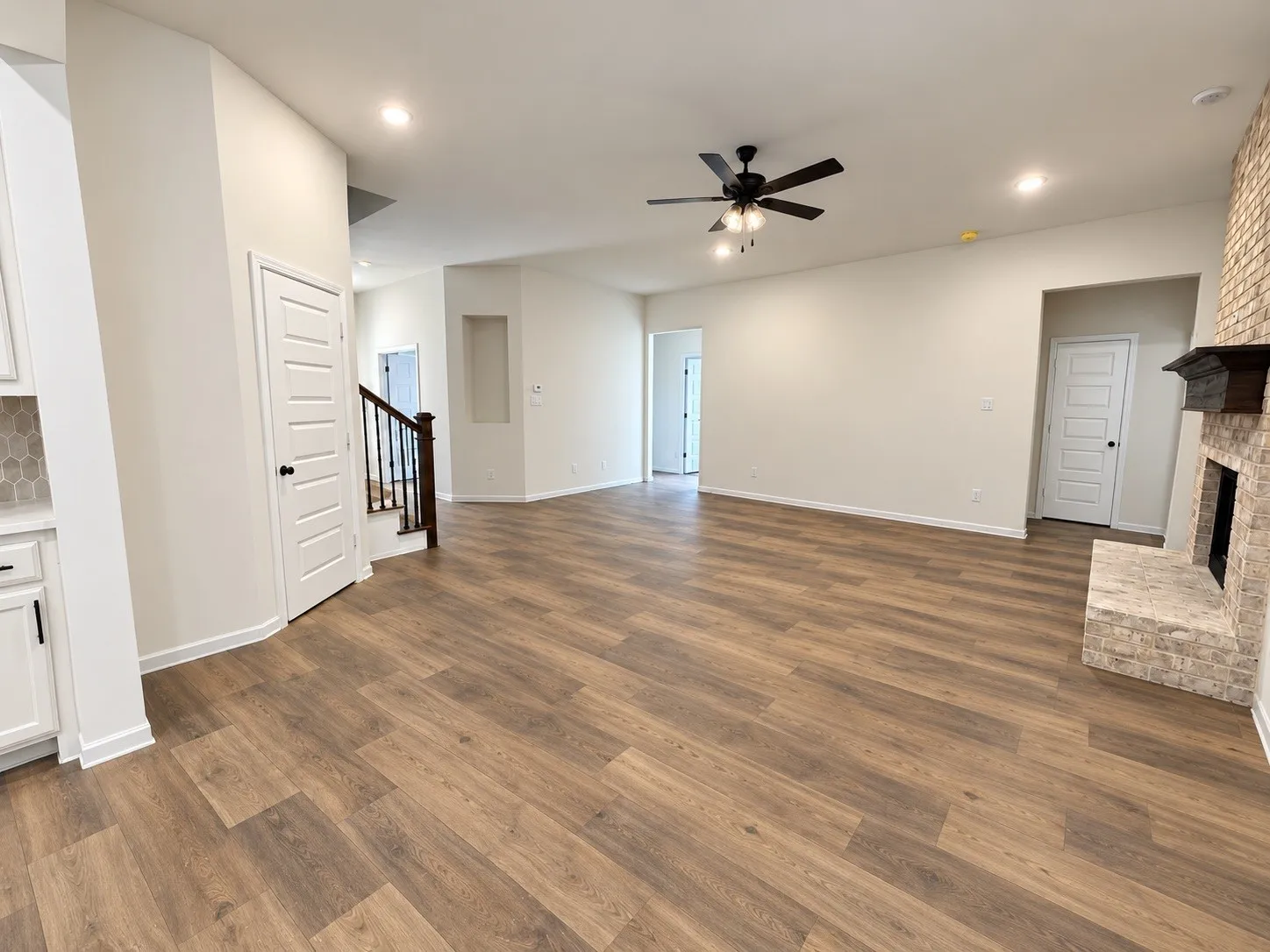 Spacious living area featuring wood-finish flooring, a stone-clad fireplace with a dark wood mantel, and a ceiling fan with integrated lighting
