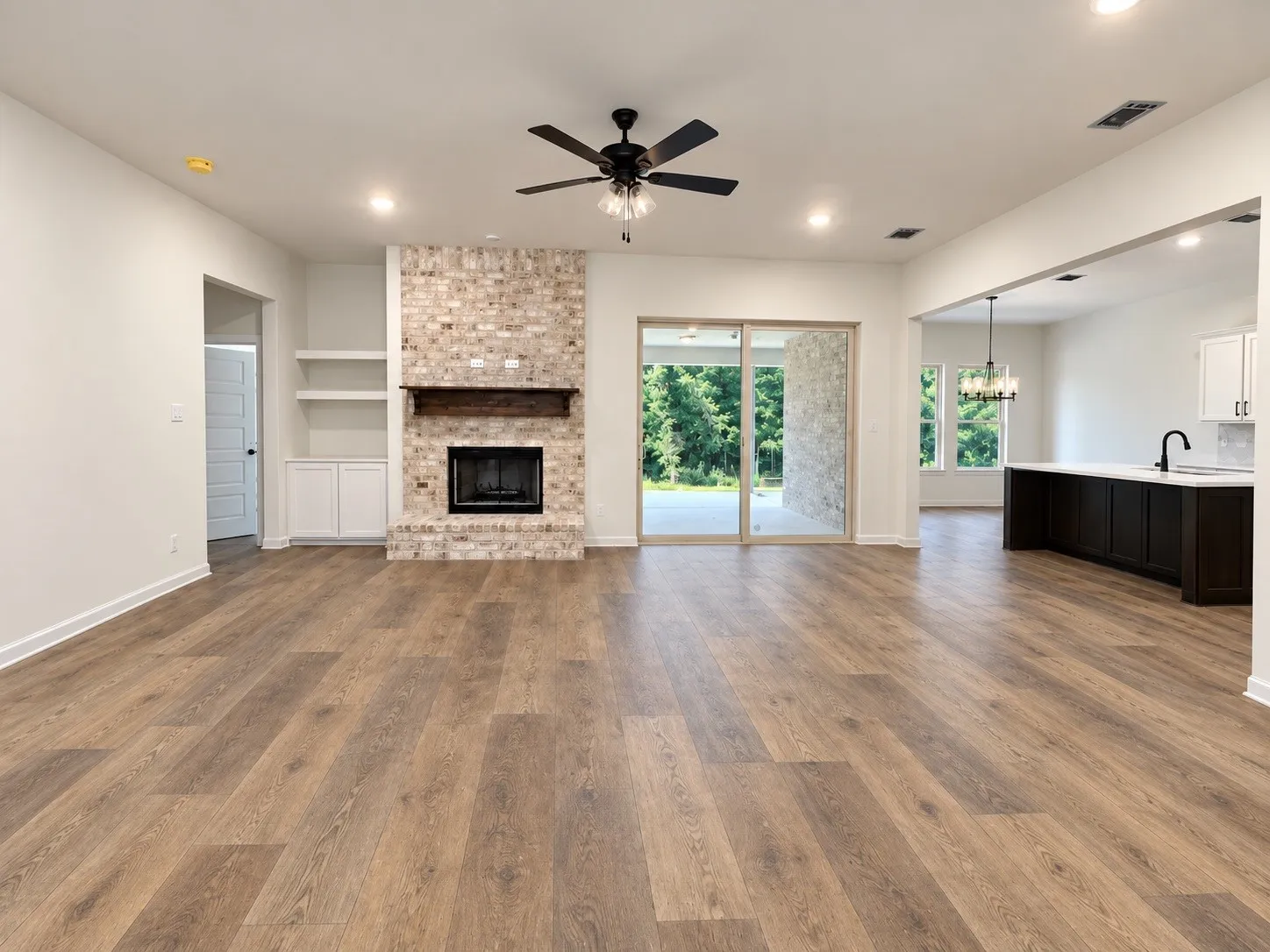 Wood-finish flooring, brick fireplace with wood mantel, built-in shelving and cabinetry, recessed lighting, and a ceiling fan