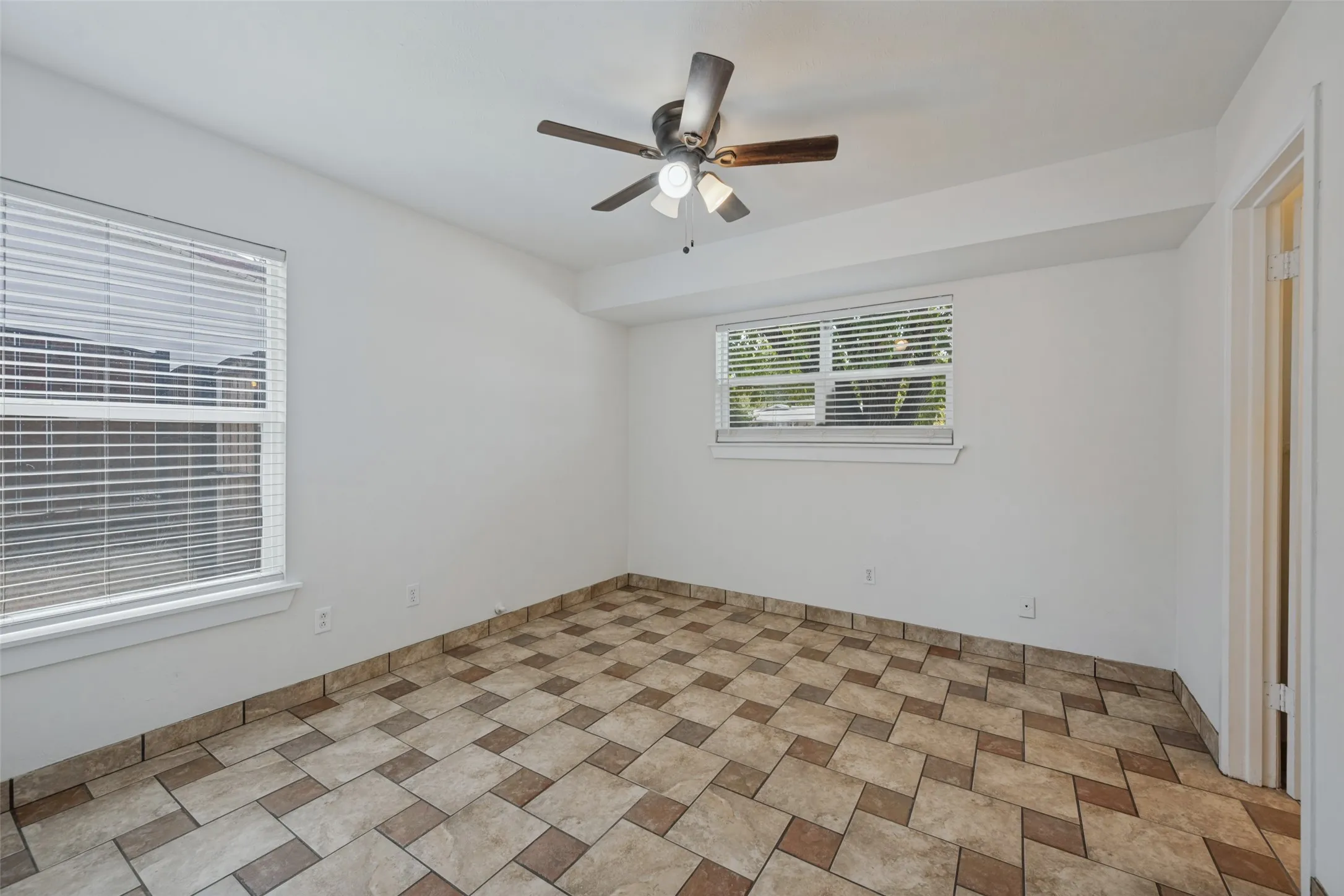 Neutral wall finishes, patterned tile flooring, a ceiling fan with integrated lighting, and multiple windows with blinds