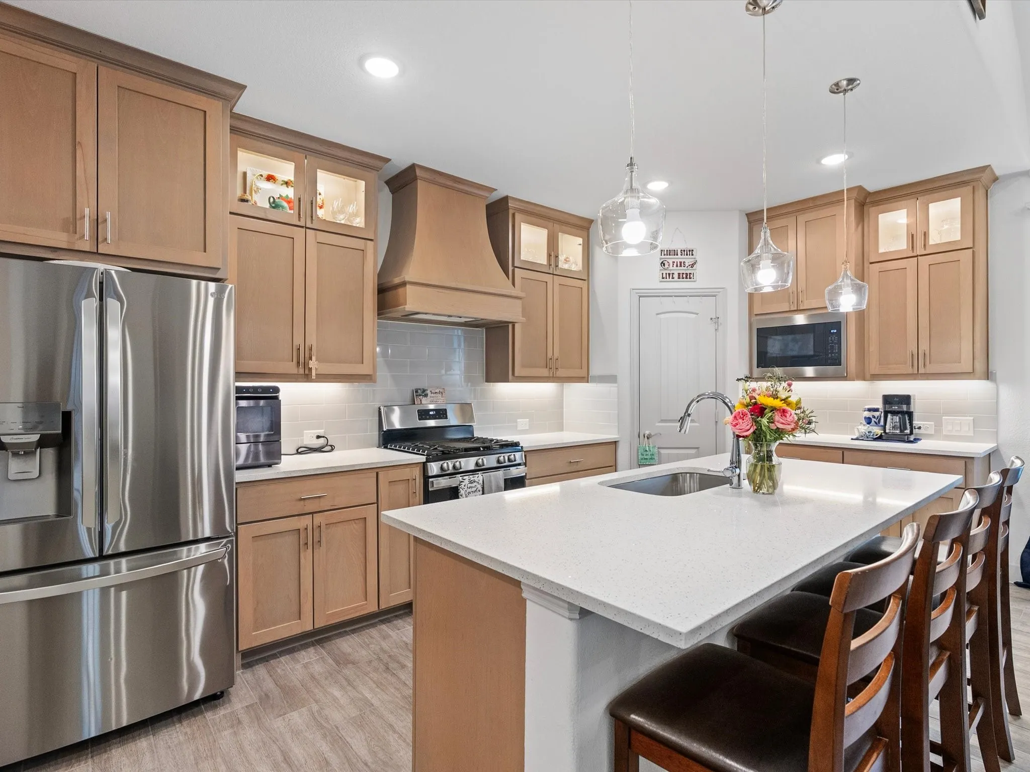 Kitchen featuring stainless steel appliances, light wood-finish cabinetry, a large kitchen island with a built-in sink, pendant lighting, and light-toned countertops