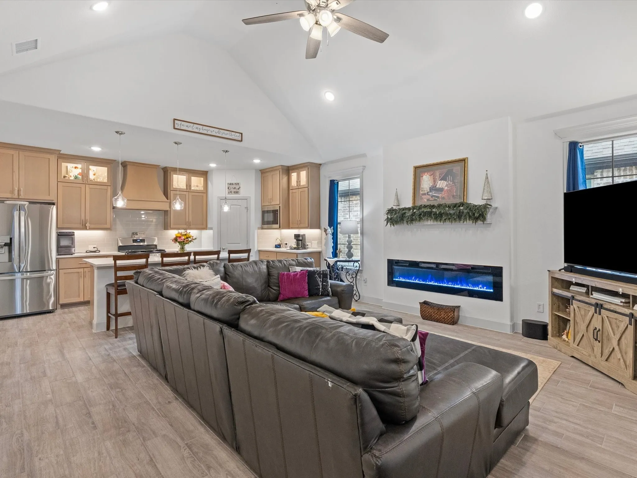 Vaulted ceiling with recessed lighting, kitchen with wood-finish cabinetry and stainless steel appliances, white subway tile backsplash, and built-in linear fireplace