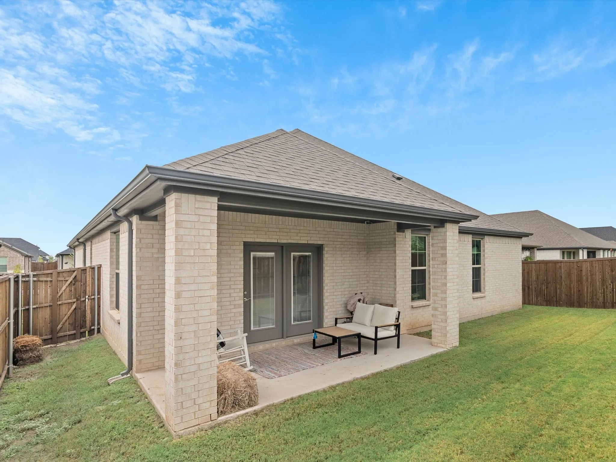 Expansive backyard featuring a covered patio, double glass-panel doors, and brick exterior