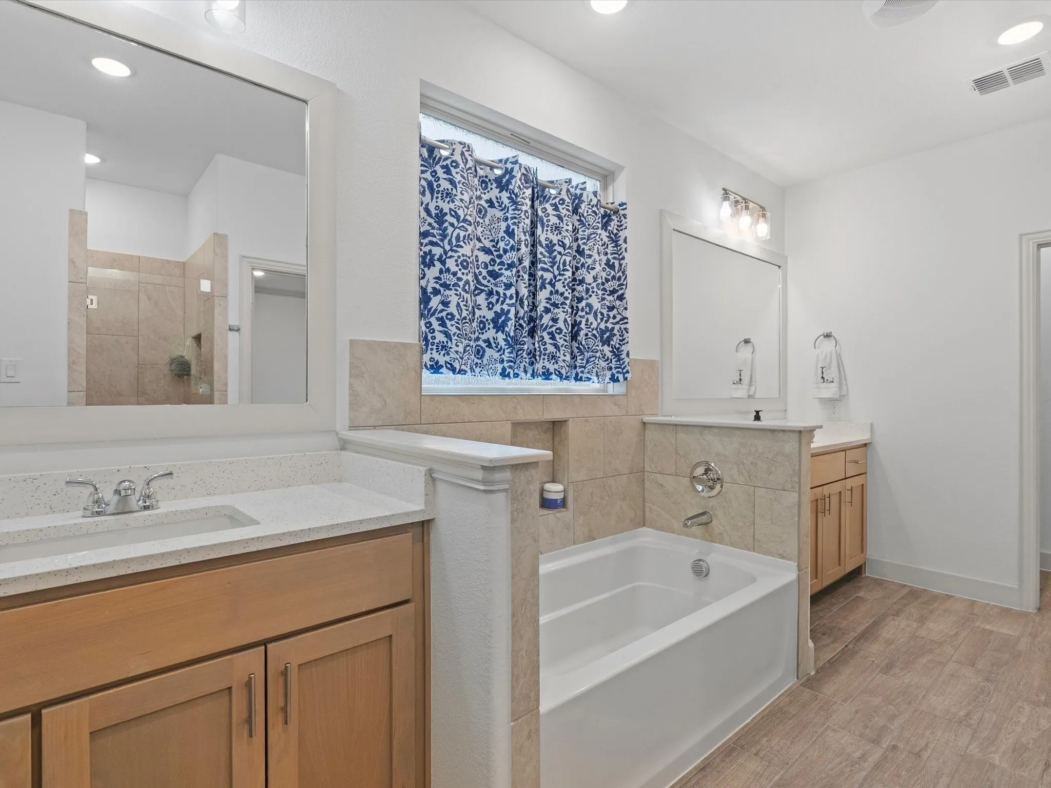 Dual vanity with quartz countertops, wood-finish flooring, a built-in soaking tub, and a separate tiled shower enclosure