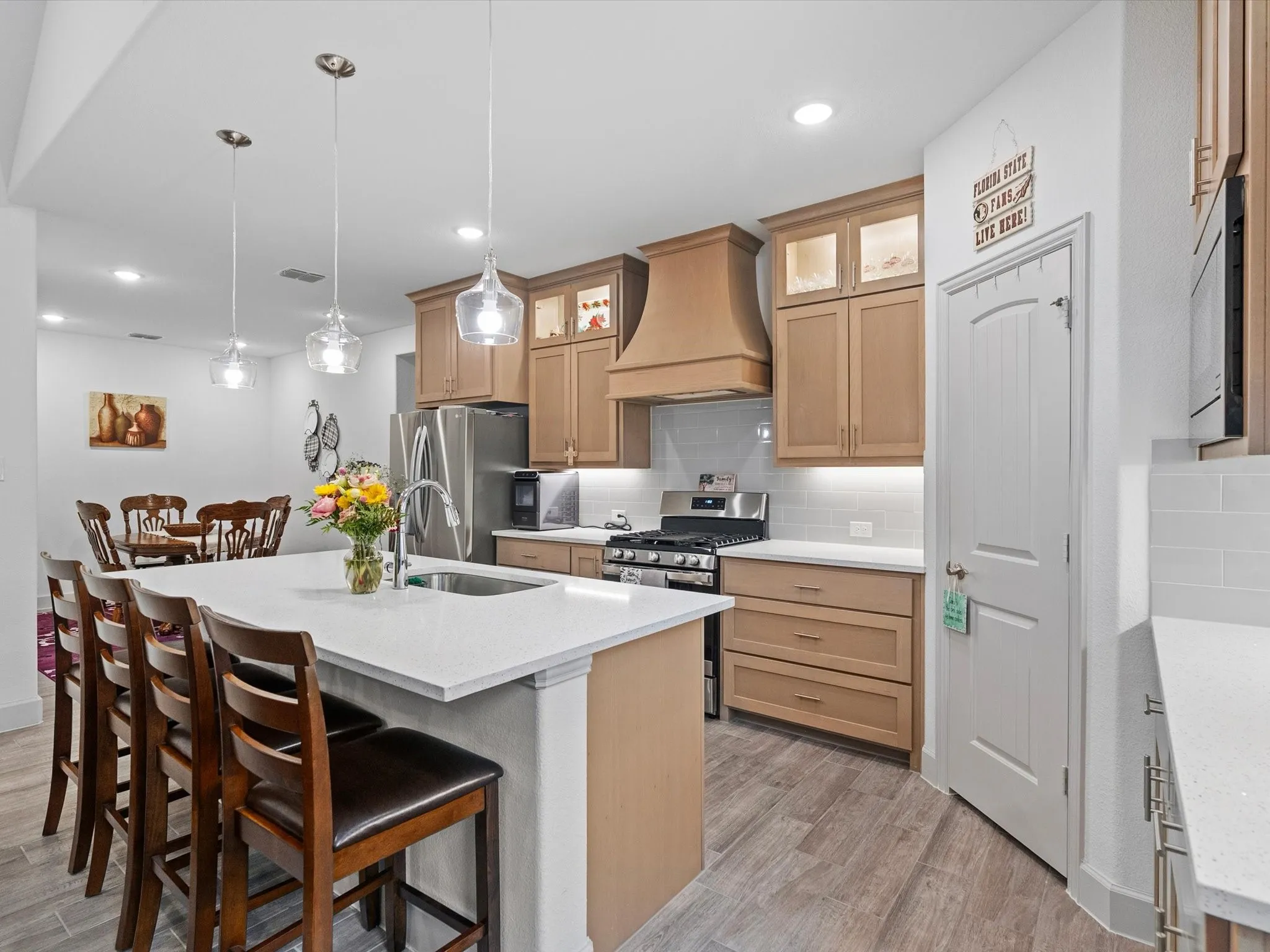 Kitchen featuring an island with built-in sink, stainless steel appliances, light wood-finish cabinetry, subway tile backsplash, and recessed lighting
