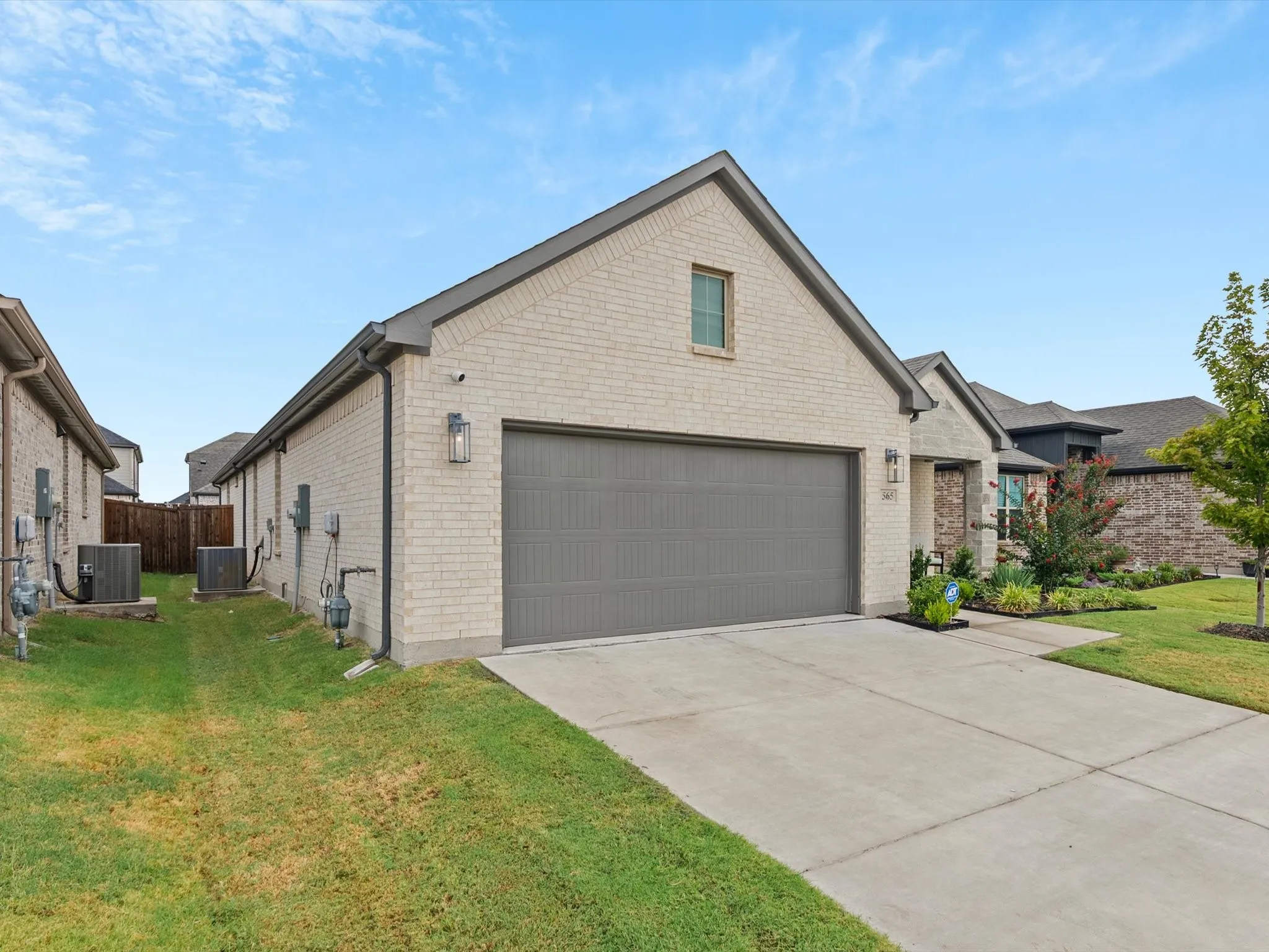 Brick exterior with a gray garage door, concrete driveway, and landscaped front yard