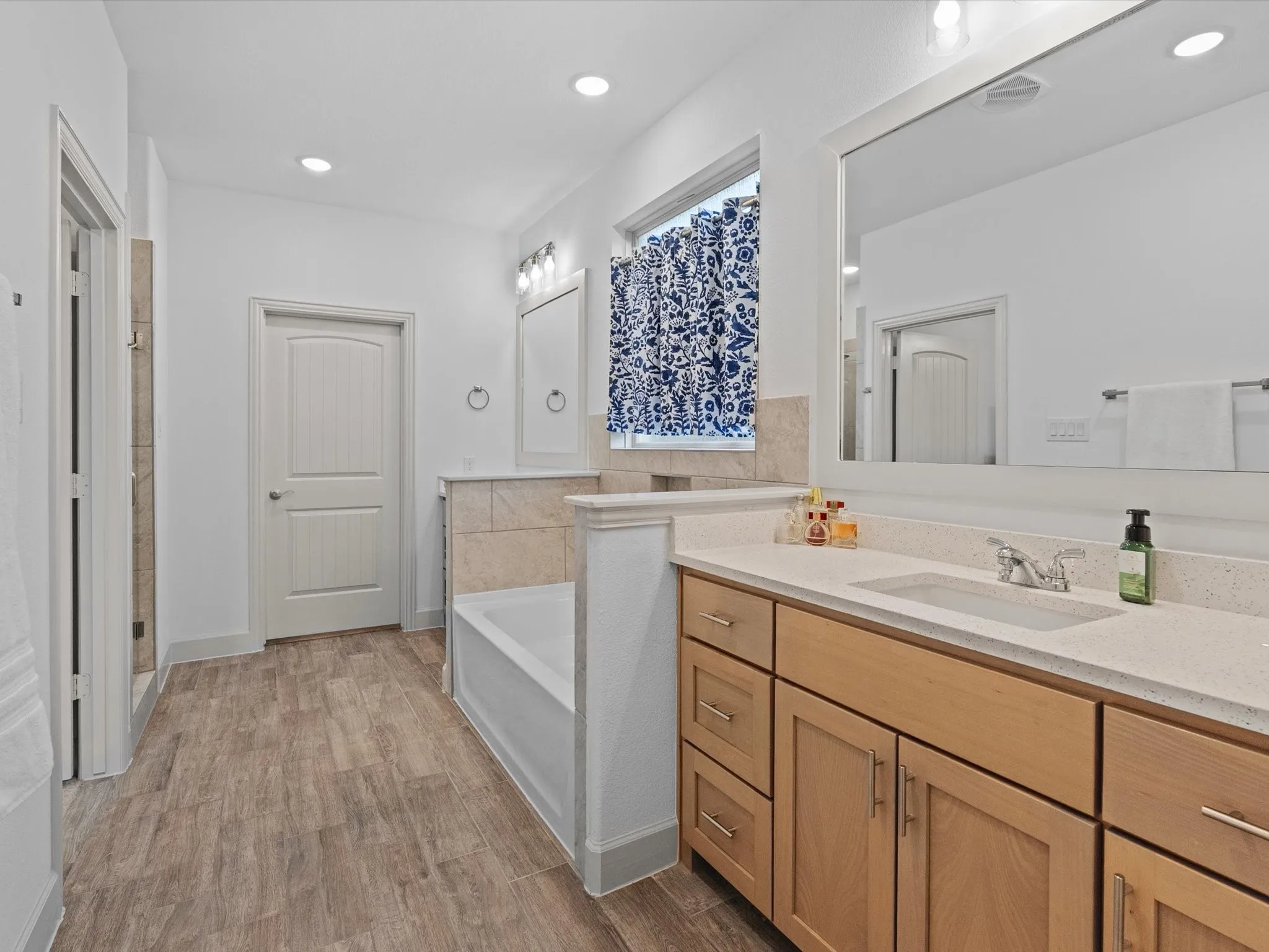 Wood-finish flooring throughout, dual sink vanity with light wood cabinetry, recessed lighting, and a built-in tub
