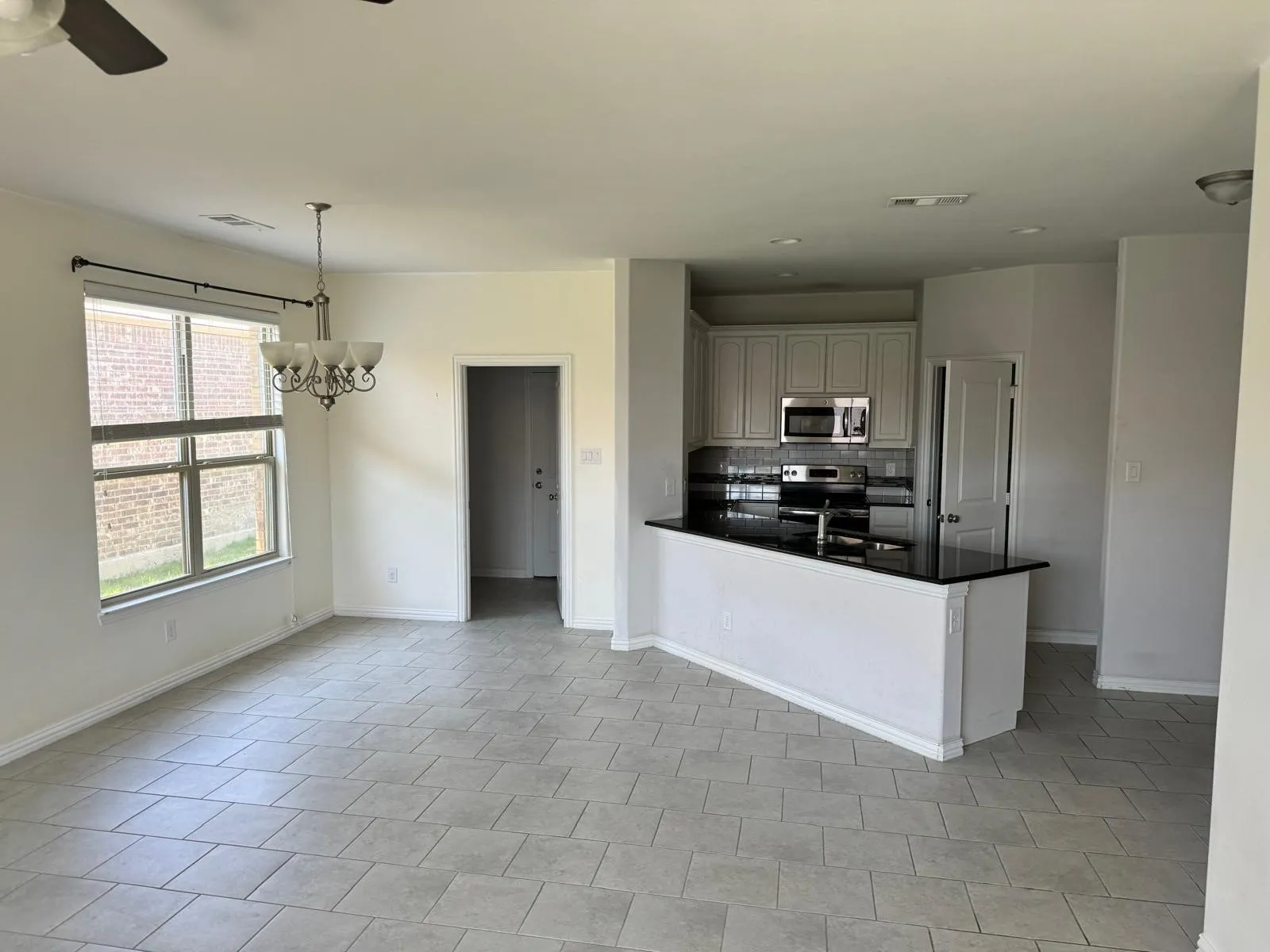 Kitchen featuring hanging light fixtures, ceiling fan with notable chandelier, appliances with stainless steel finishes, tasteful backsplash, and light tile floors