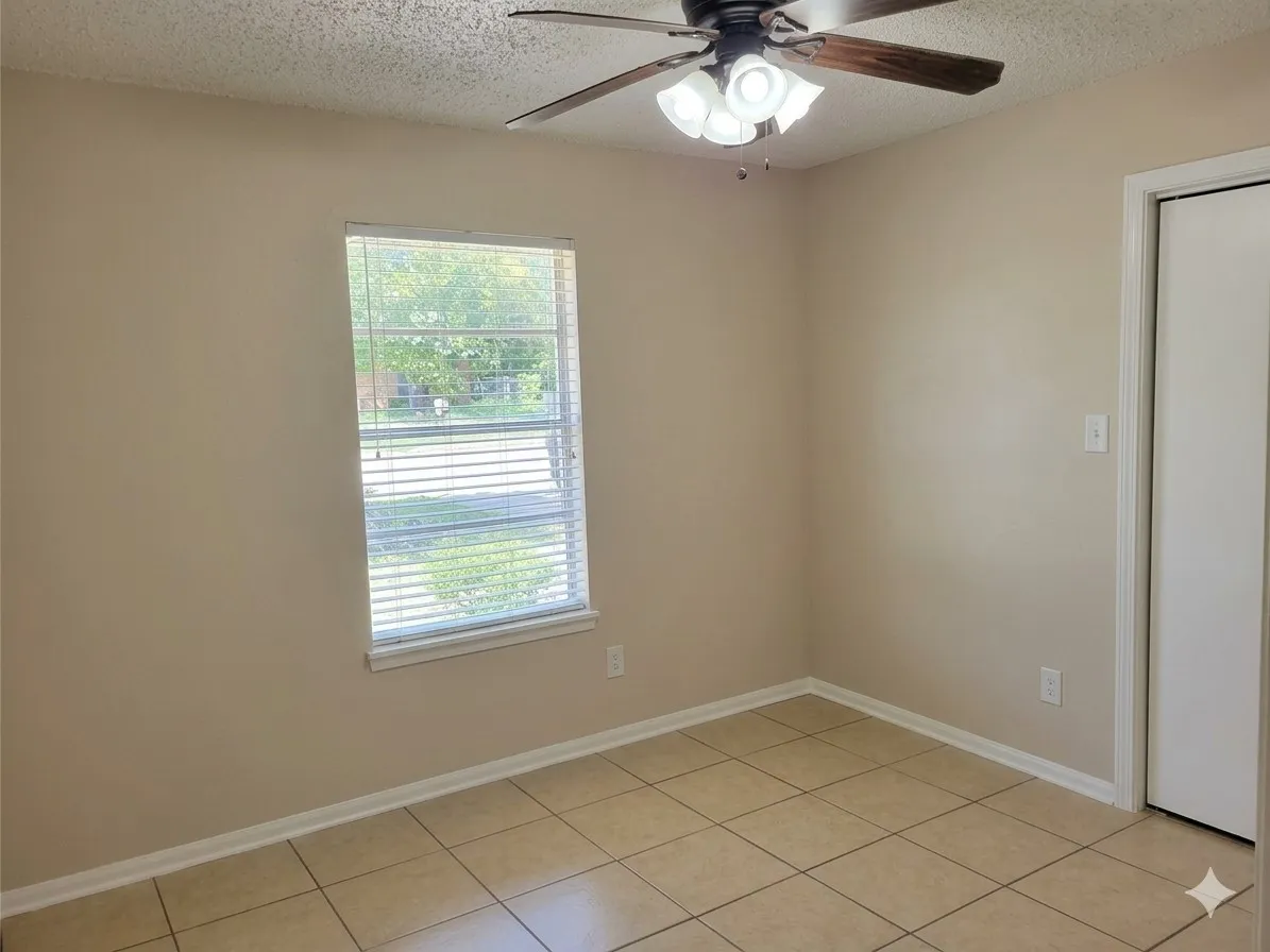Neutral tone wall paint, tile flooring, window with blinds, ceiling fan with integrated lighting, and a white bi-fold closet door