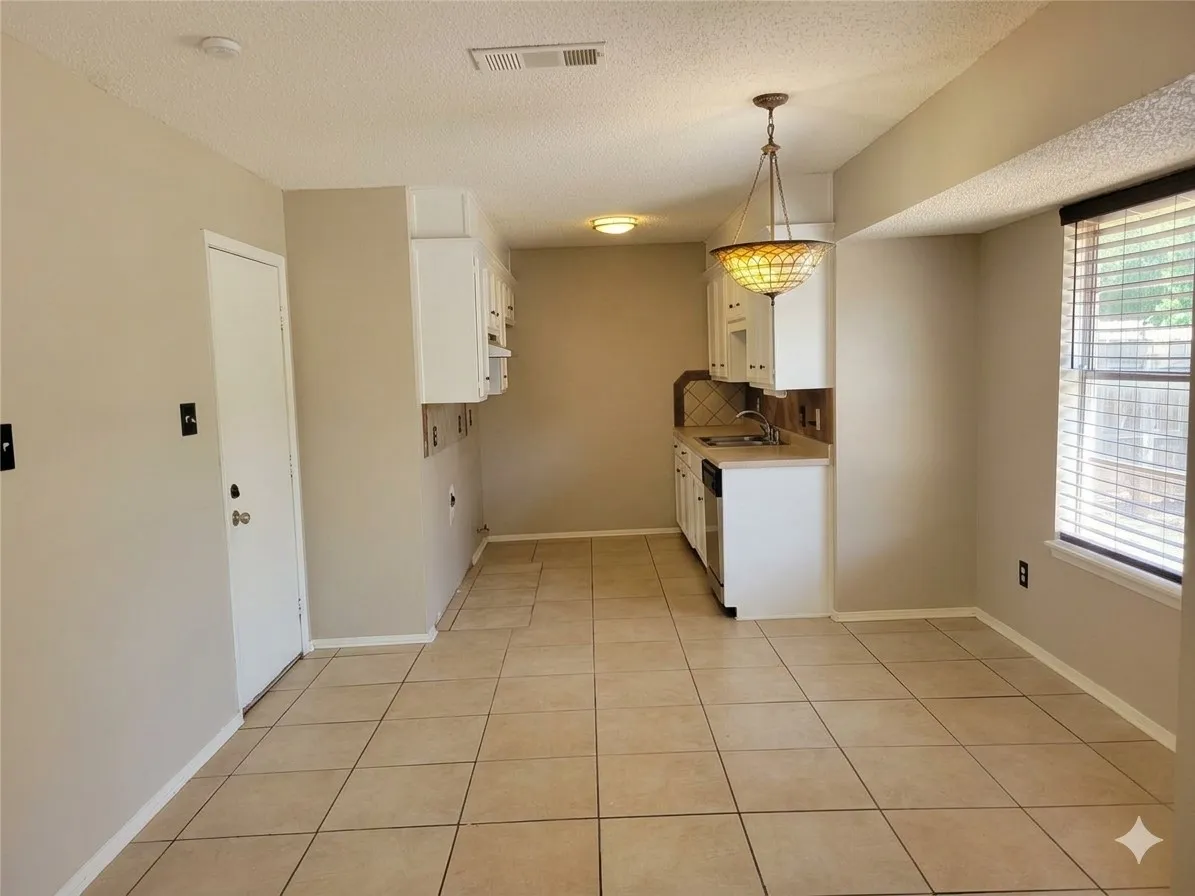 Tile flooring, white cabinetry, integrated sink, built-in dishwasher, and a decorative pendant light
