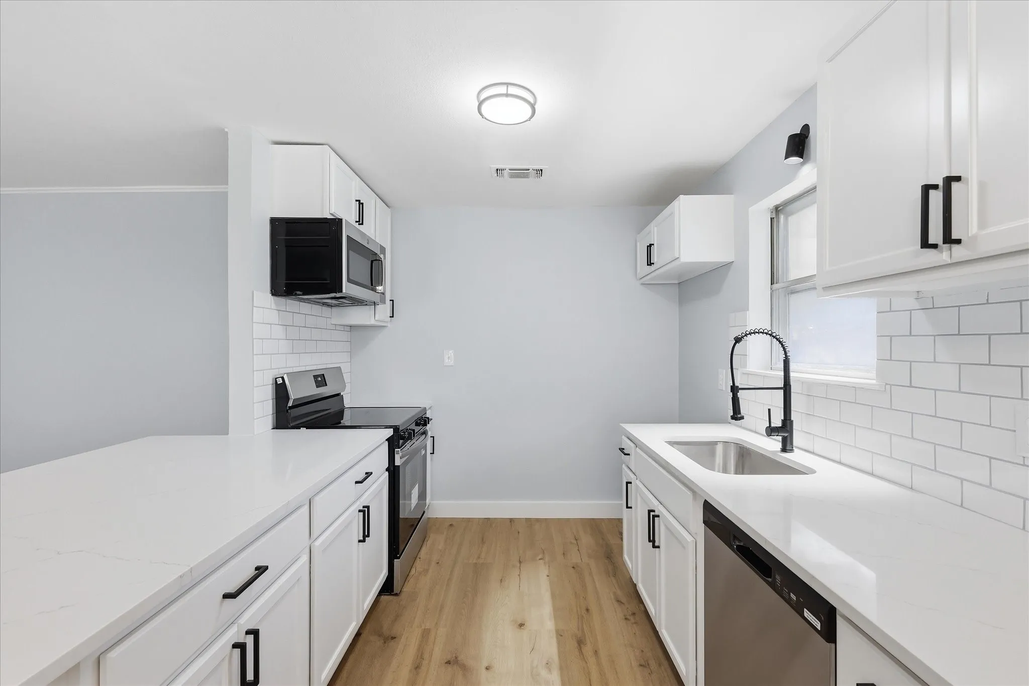 Modern galley kitchen featuring white cabinetry with black hardware, white subway tile backsplash, and light wood-finish flooring