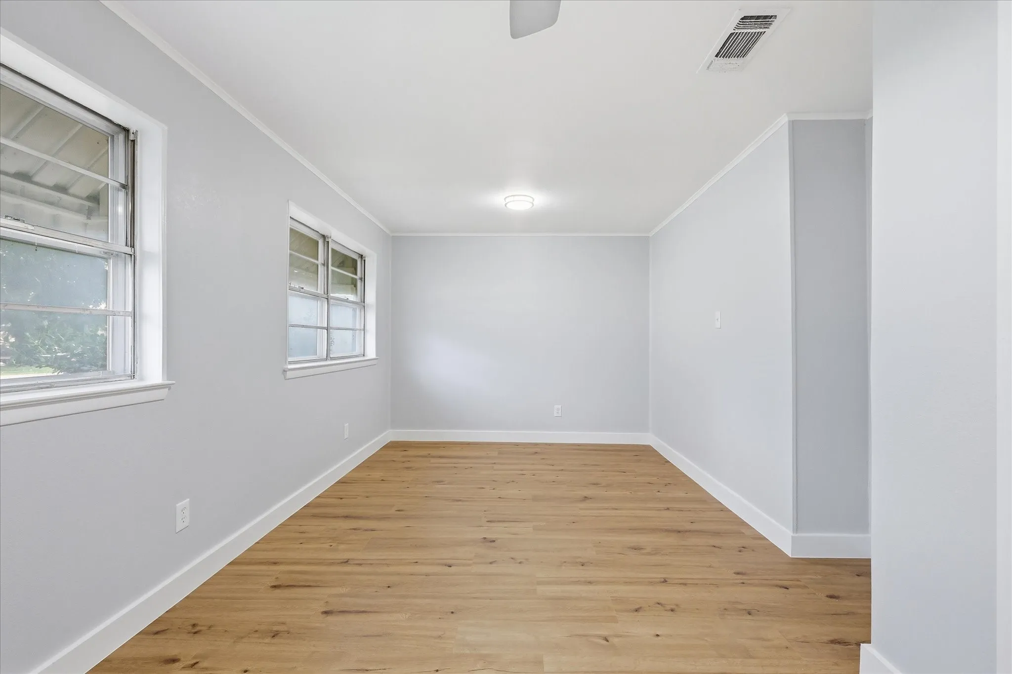 Spacious room featuring wood-finish flooring, light gray walls, white trim, two windows, and overhead lighting