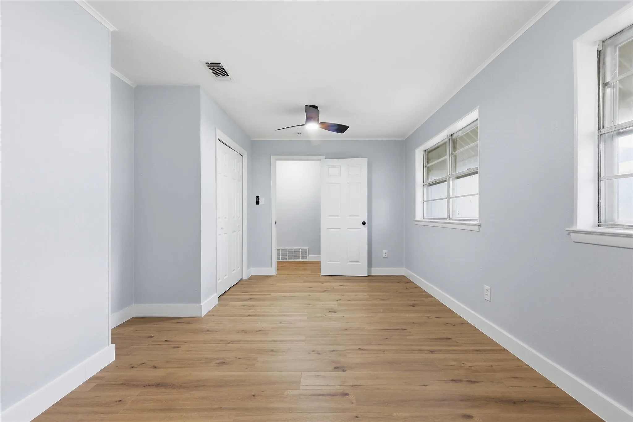 Spacious room featuring wood-finish flooring, light blue wall paint, and white trim