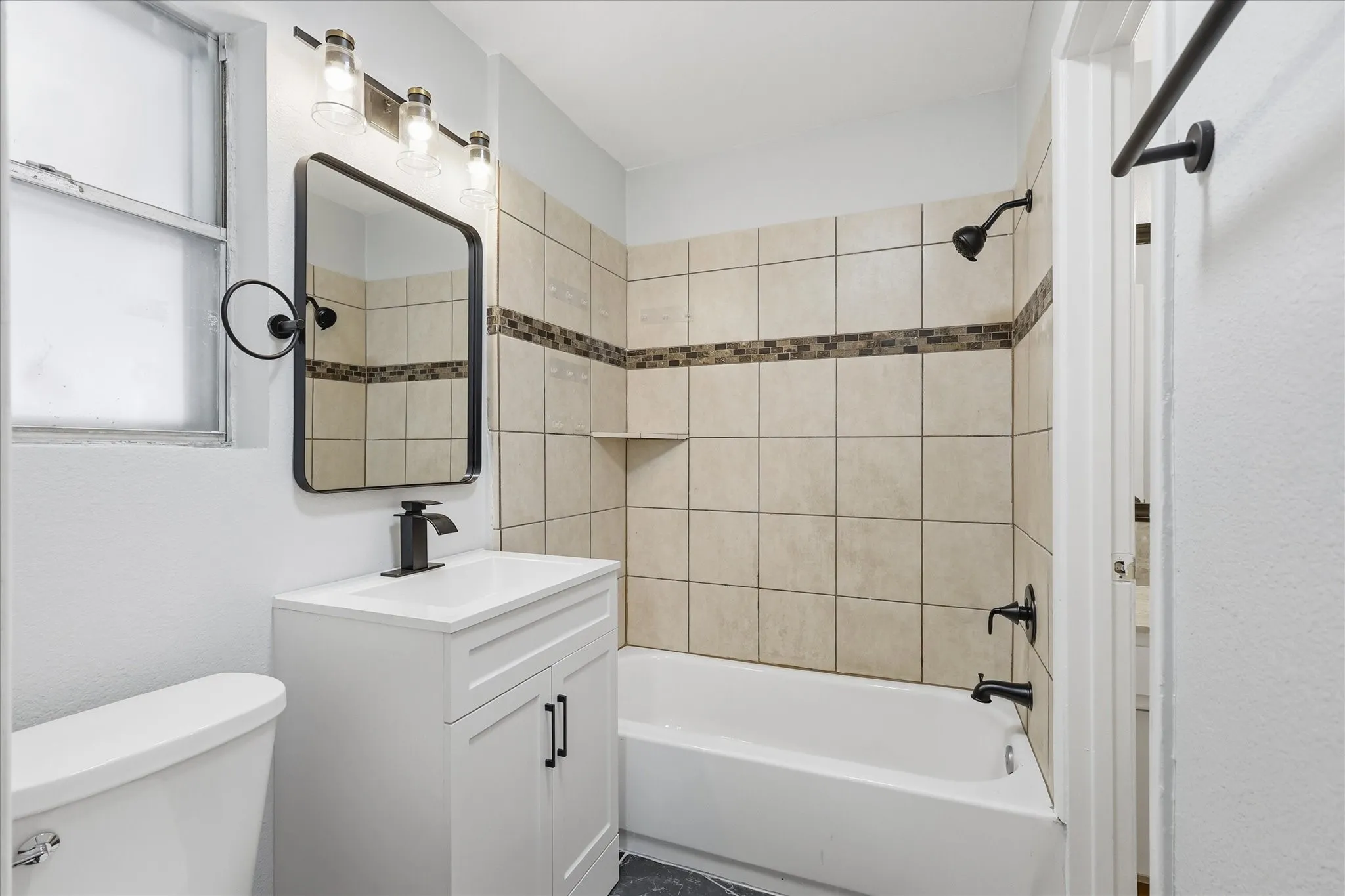Bathroom featuring a white vanity with integrated sink, black fixtures, and a rectangular mirror