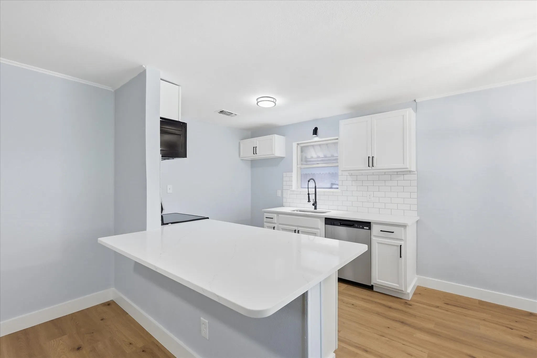 Modern kitchen featuring a white countertop island, white cabinetry with black hardware, a subway tile backsplash, and wood-finish flooring