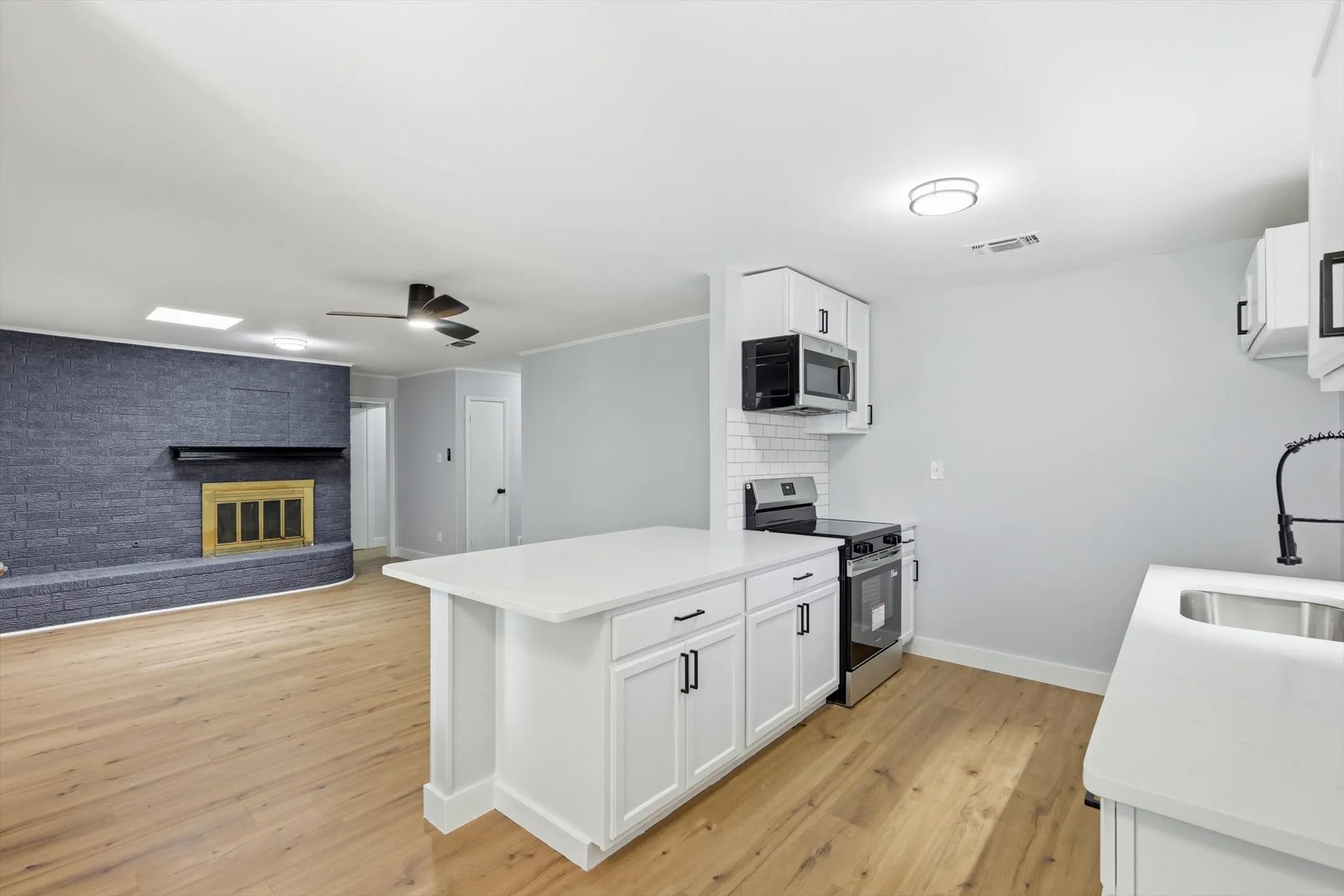 Open-concept living area with wood-finish flooring, a prominent blue brick fireplace, and a contemporary kitchen island