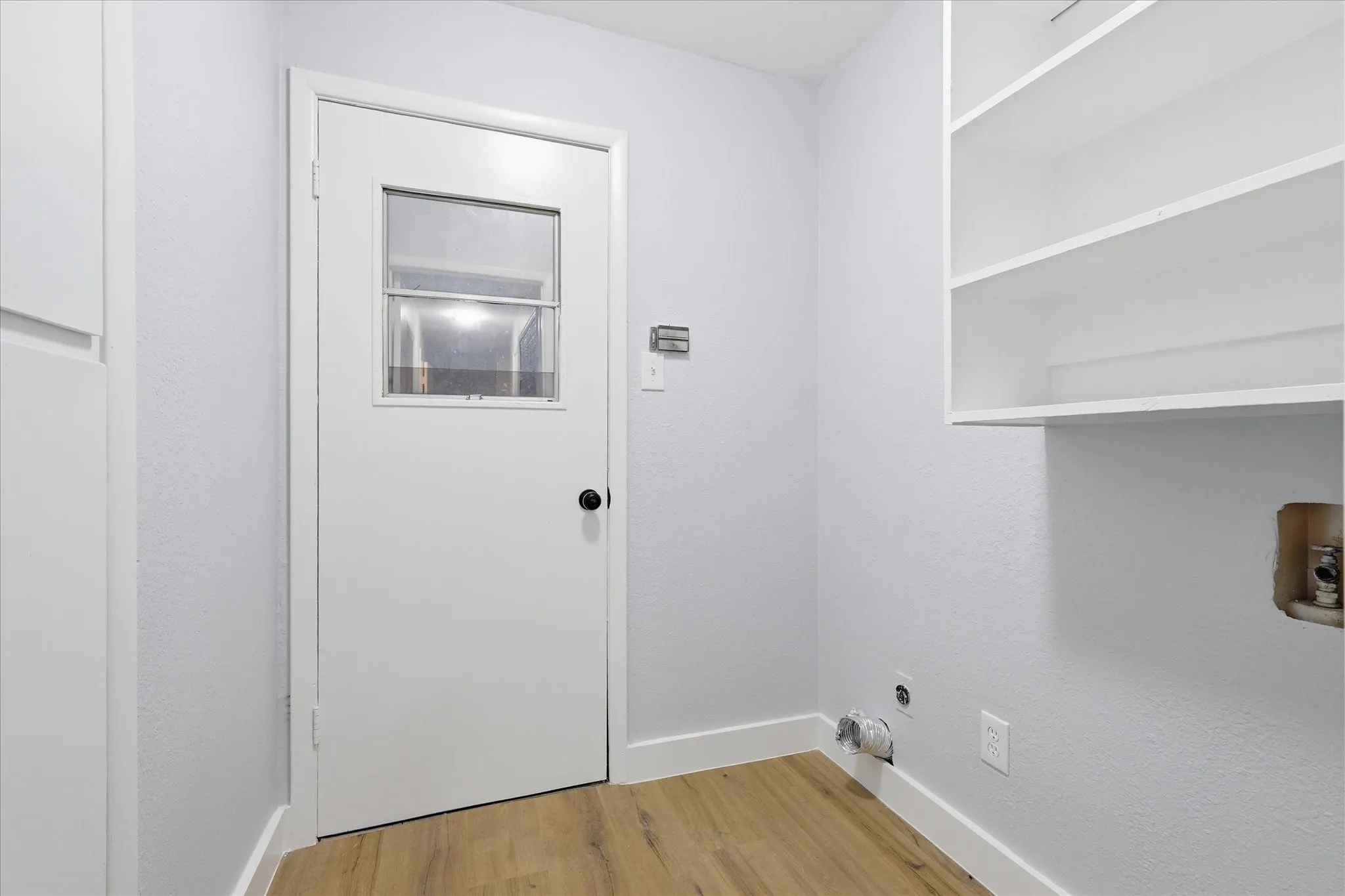 Utility area featuring wood-finish flooring, a white door with a window insert, and built-in shelving