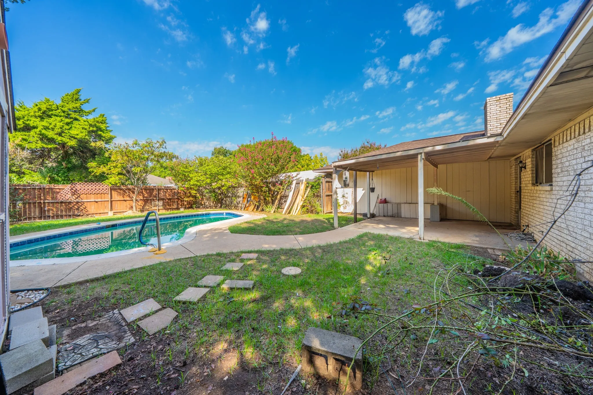 In-ground swimming pool with integrated steps, concrete patio surround, and a metal handrail
