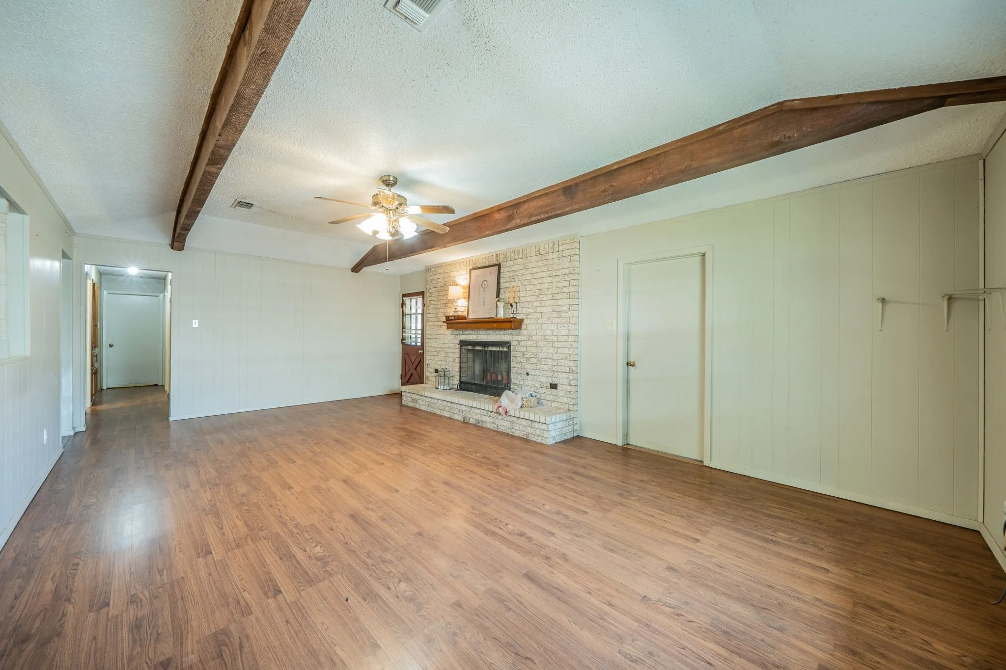 Expansive living area with wood-finish flooring, exposed ceiling beams, and a brick-faced fireplace