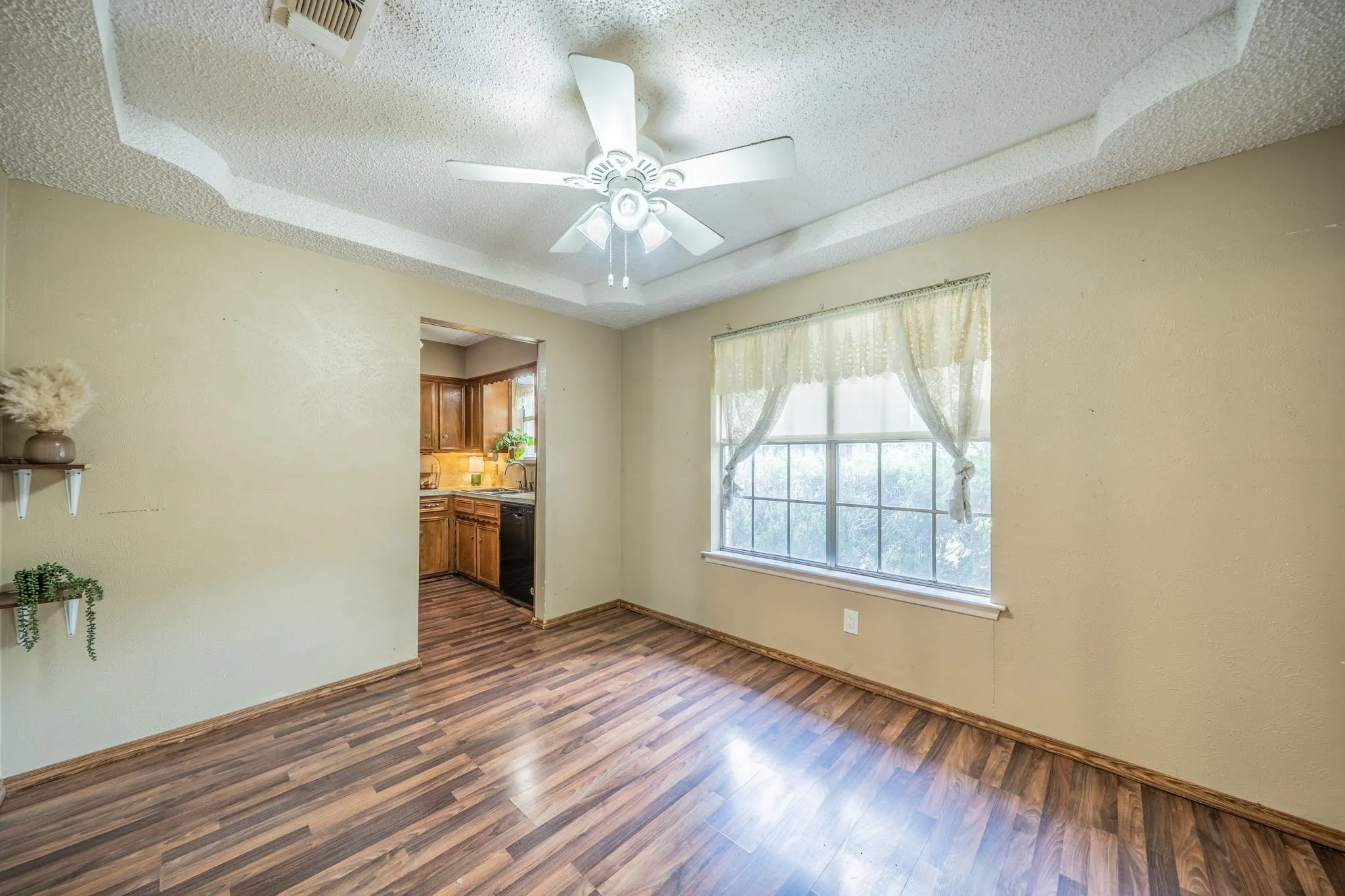 Tray ceiling with a ceiling fan, wood-finish flooring, and a large window
