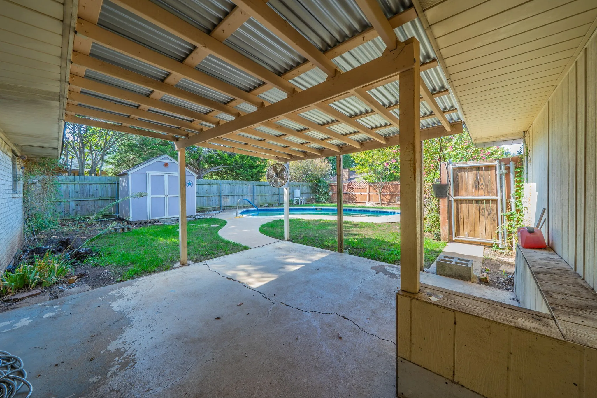 Covered patio with concrete flooring, wood privacy fencing, a storage shed, and an inground swimming pool