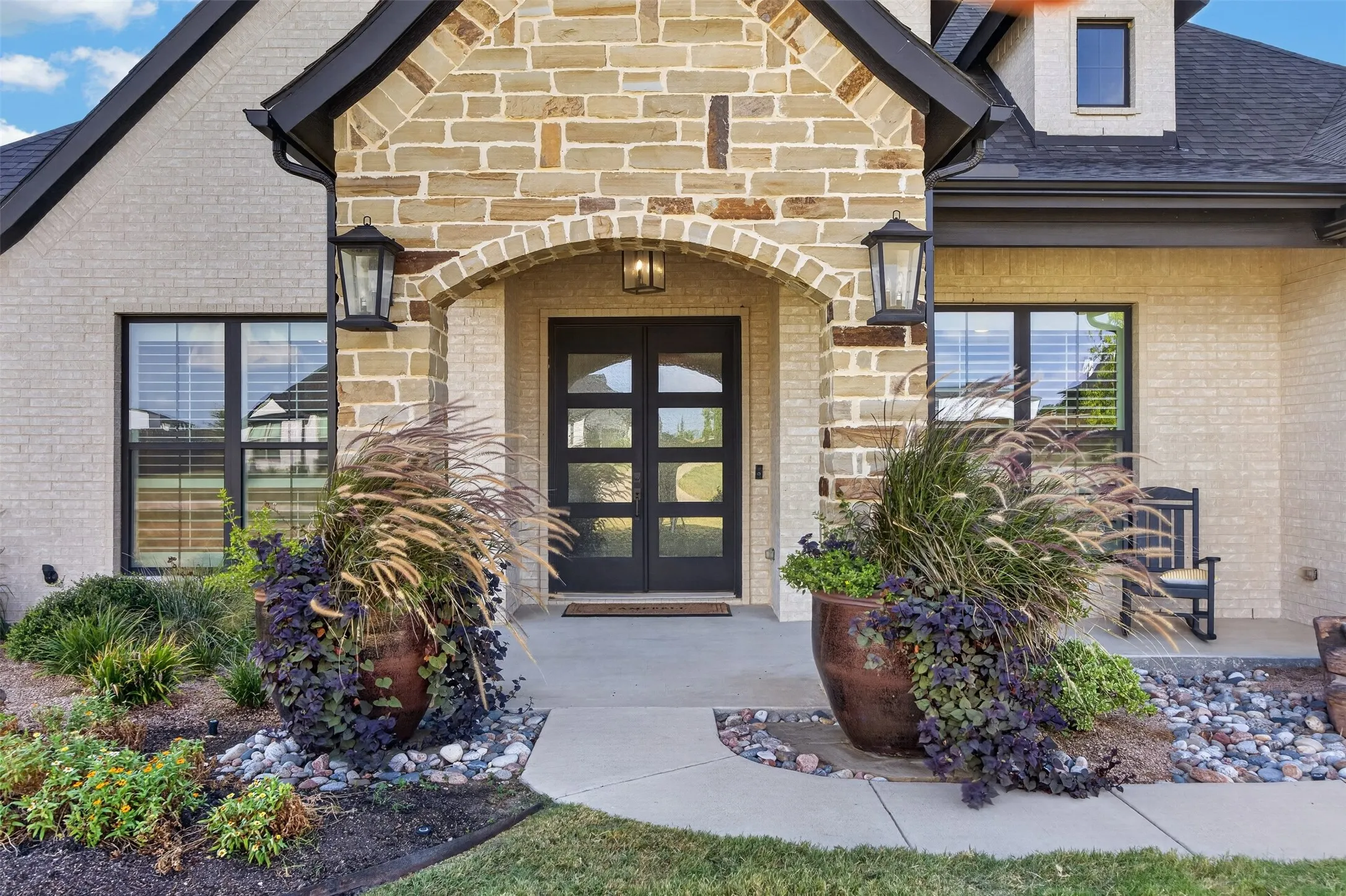 Inviting entry with stone porch, double doors, large irrigated planters and professional landscaping