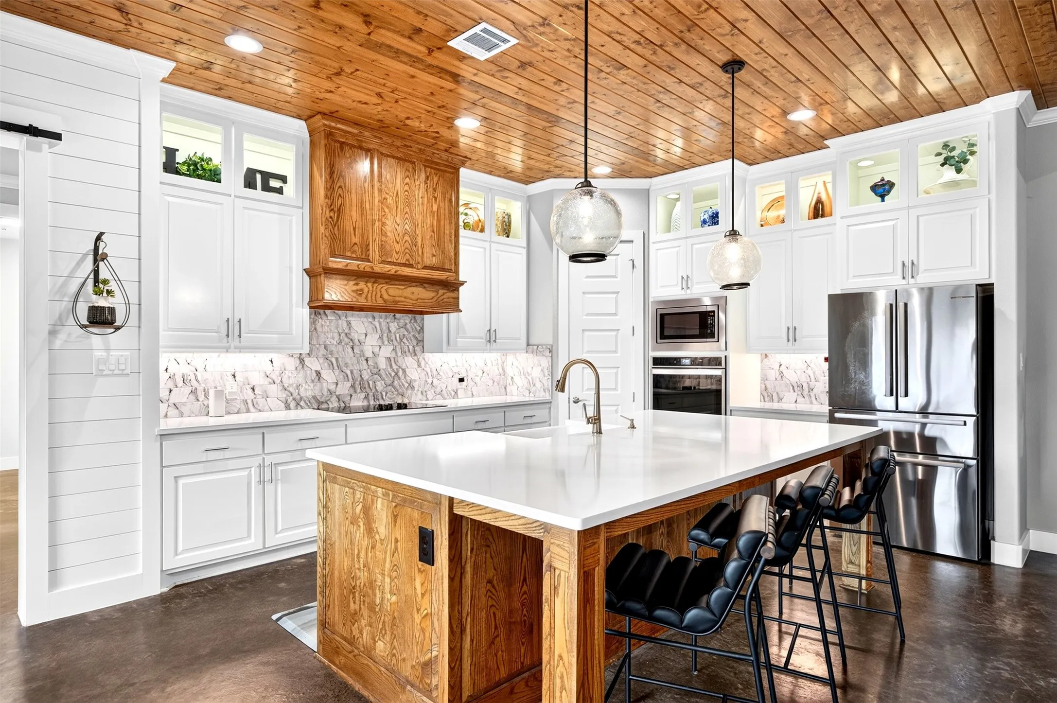 Designer kitchen with oversized island, farmhouse sink, glass and lighted upper cabinets, stunning backsplash, double ovens, custom wood ceiling