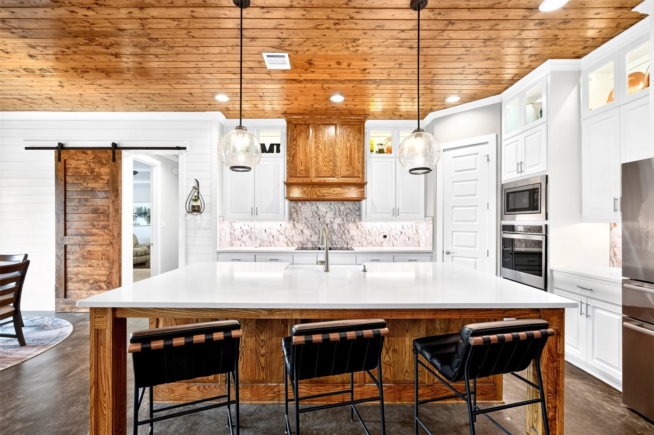 Show stopping kitchen with wood ceilings, oversized island, farmhouse sink, pendant lighting, lighted and glass upper cabinets