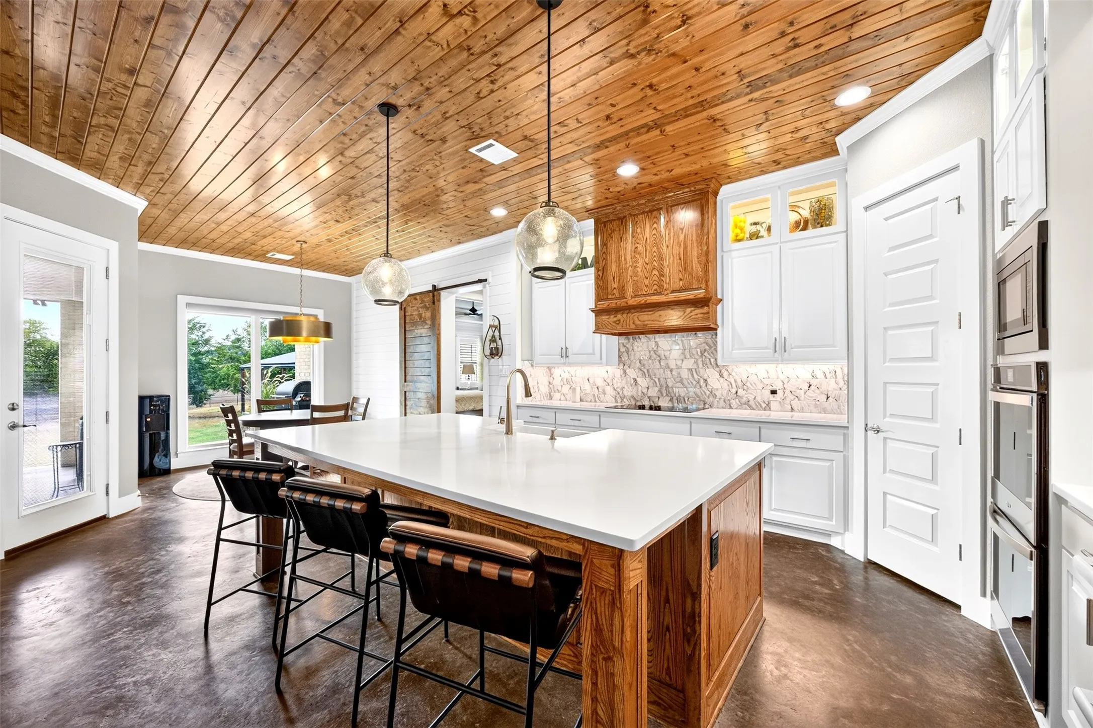 Show stopping kitchen with wood ceilings, oversized island, farmhouse sink, pendant lighting, lighted and glass upper cabinets
