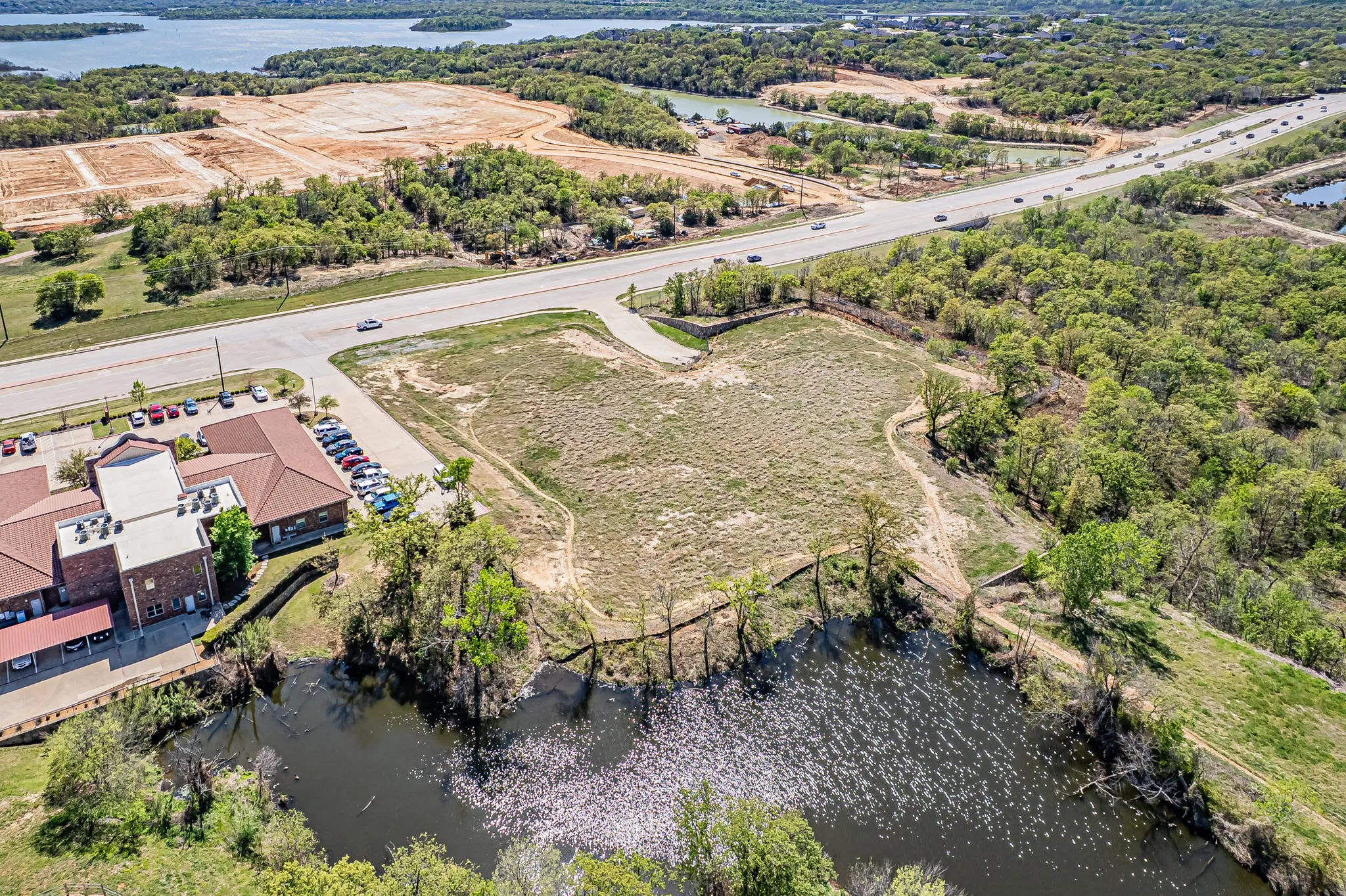 Waterfront land parcel with direct road access, adjacent to developed commercial property, and surrounded by mature trees