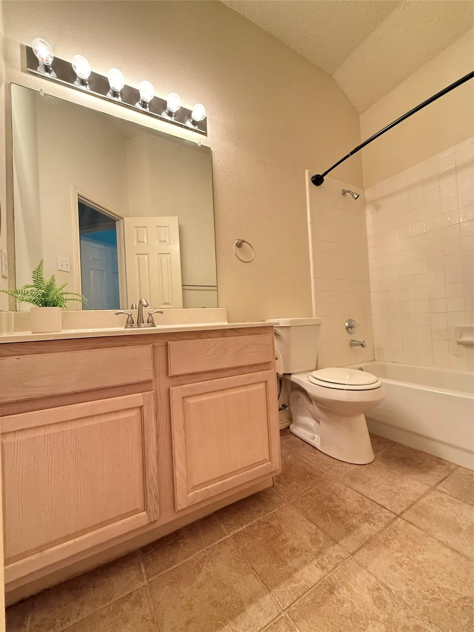 Single vanity with wood-finish cabinetry, tile flooring, and a shower-tub combination with white subway tile surround
