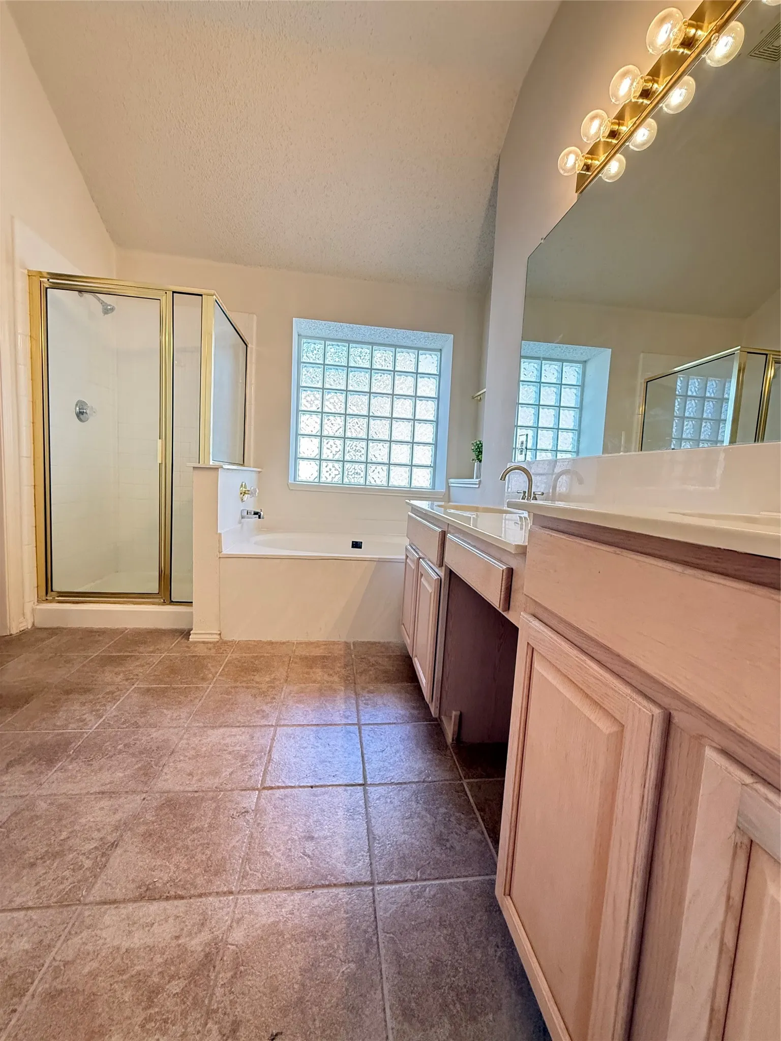 Dual vanity with integrated sinks, a built-in bathtub, glass block window, and a separate shower enclosure with a gold-finish frame