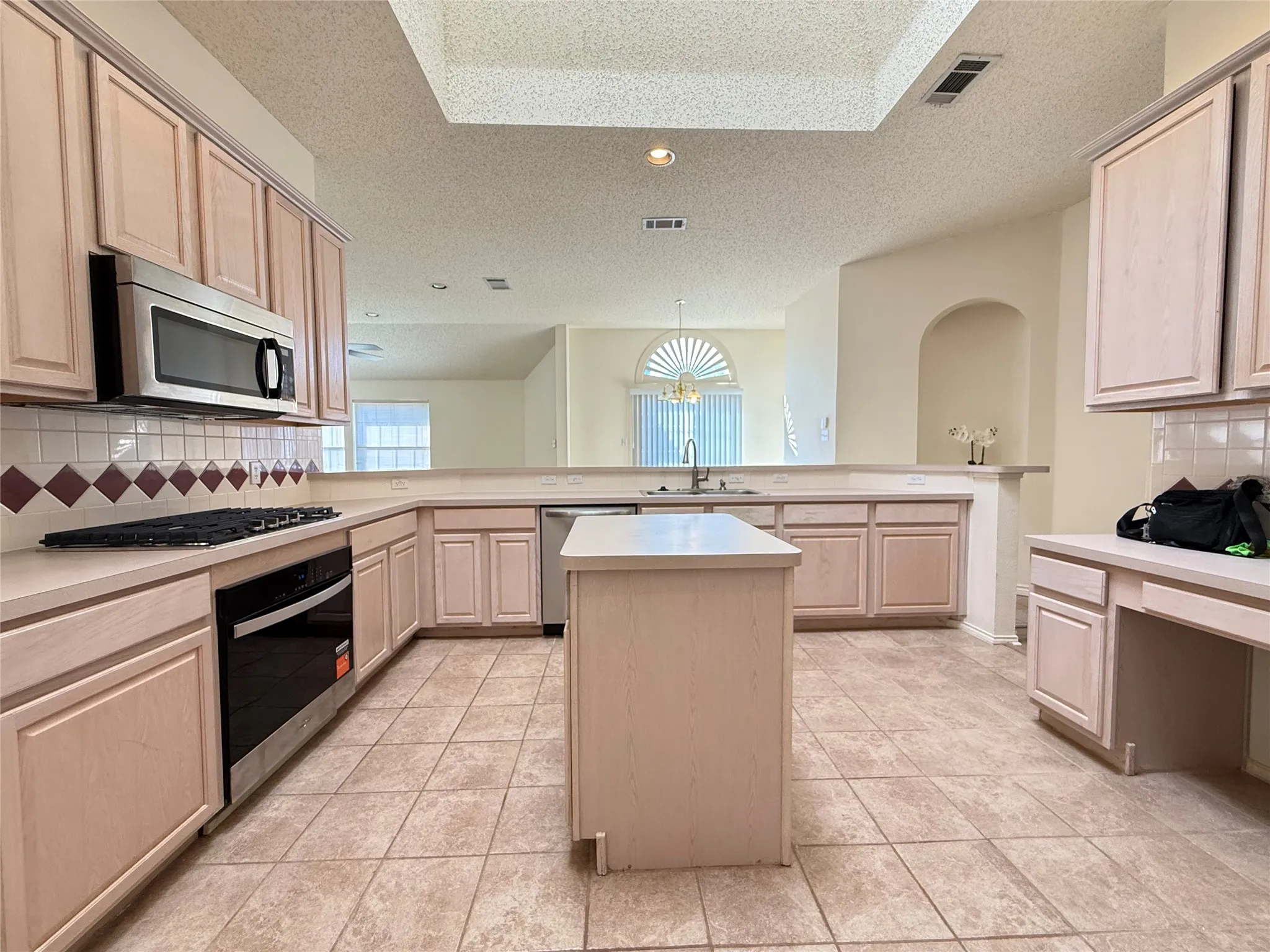 Spacious kitchen featuring an island, integrated stainless steel appliances, tile flooring, and a tile backsplash with decorative accents