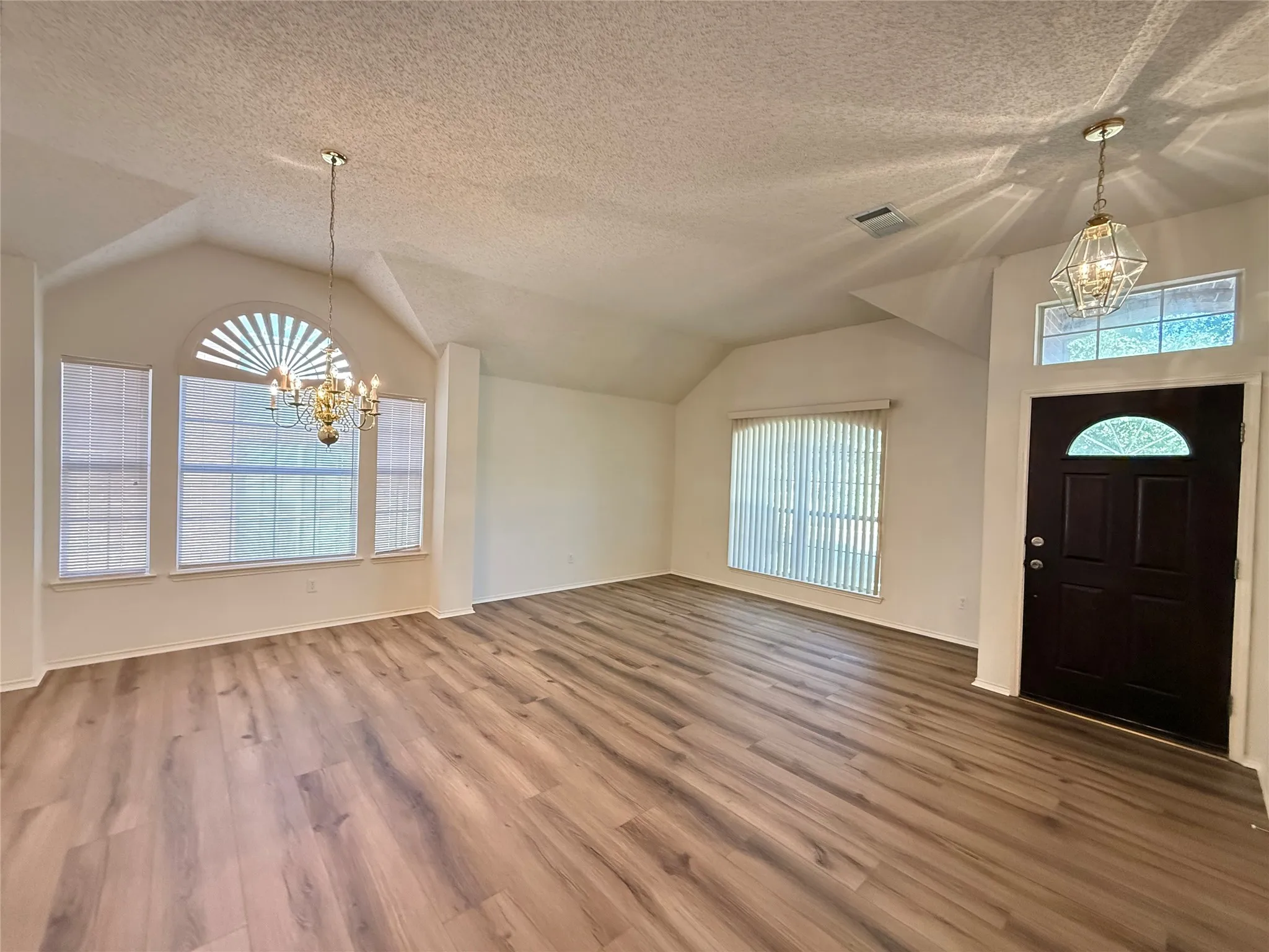 Vaulted ceilings, wood-finish flooring, and multiple windows with blinds