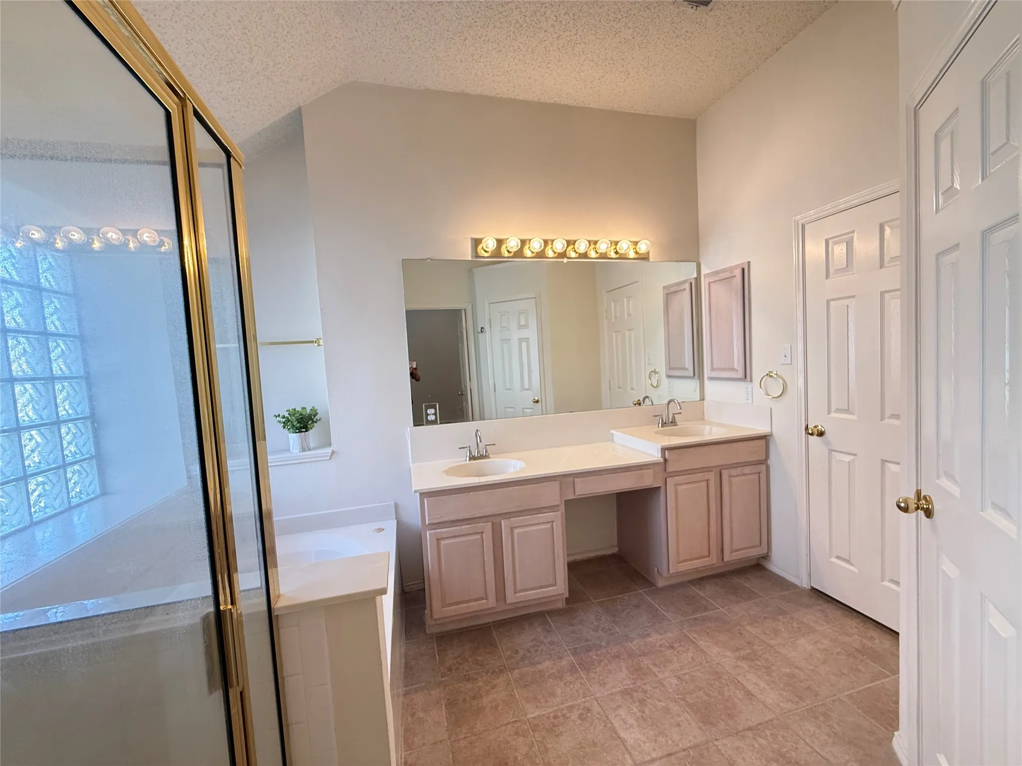 Dual vanity with integrated sinks, expansive mirror with task lighting, tiled flooring, and an adjacent glass-enclosed shower with glass block accent